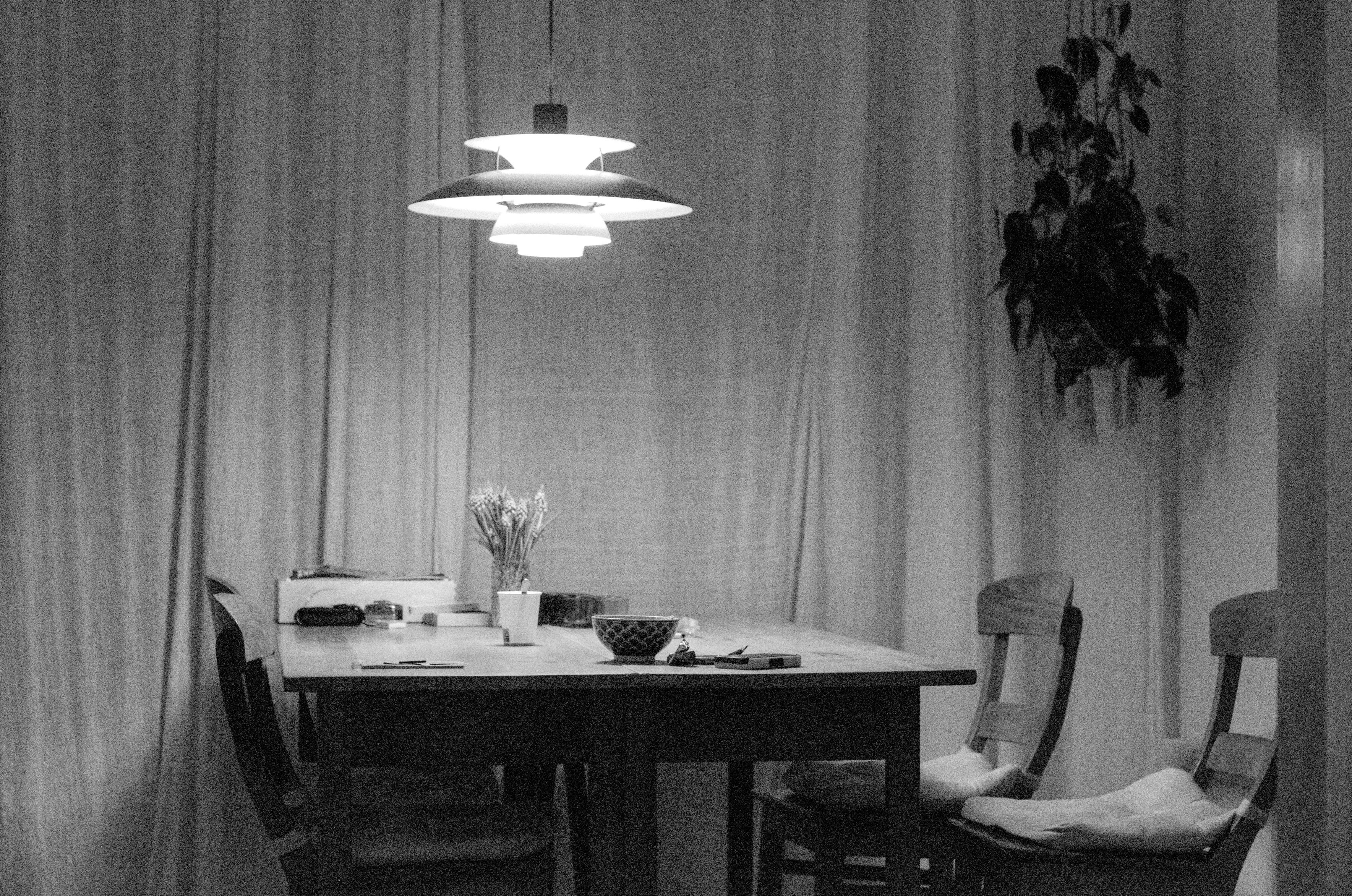 Black and white photo of a table with four chairs around it. Above the table hangs a lamp that is blown out to white.