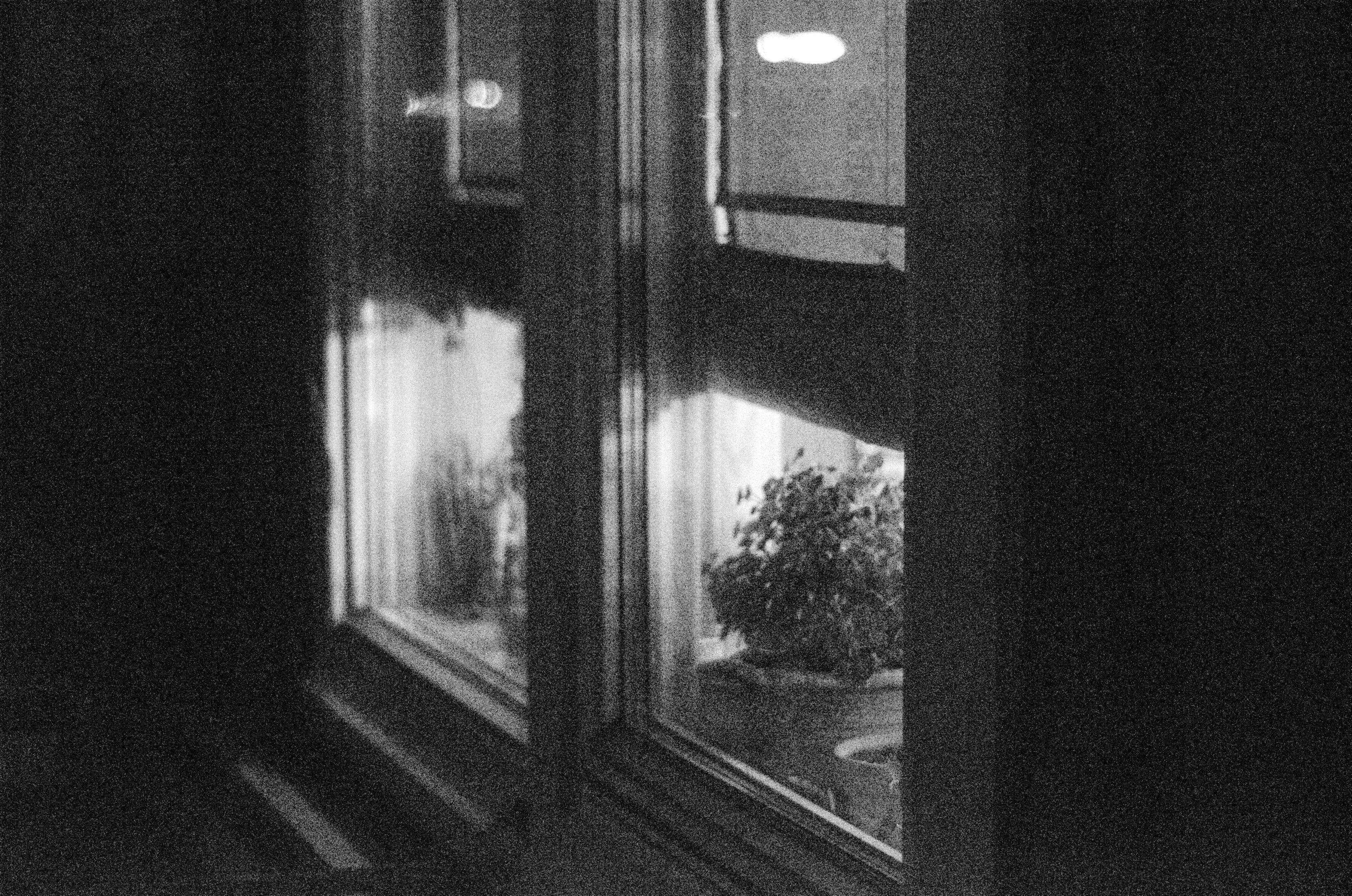 Black and white photo from outside looking at two windows into the lit interior.