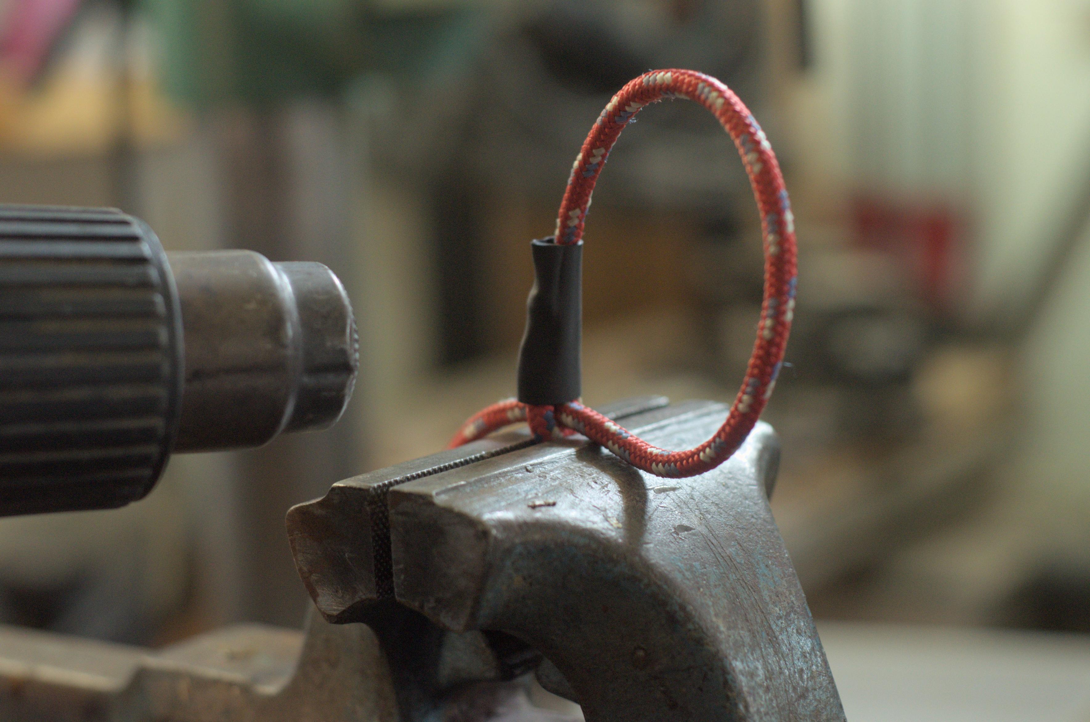 Shrinking the black tube around the sewn joint, which is held at the tip in a big bench vice. A heat gun is pointed at the halfway shrunken tubing, which is starting to conform to the shape of the joint.