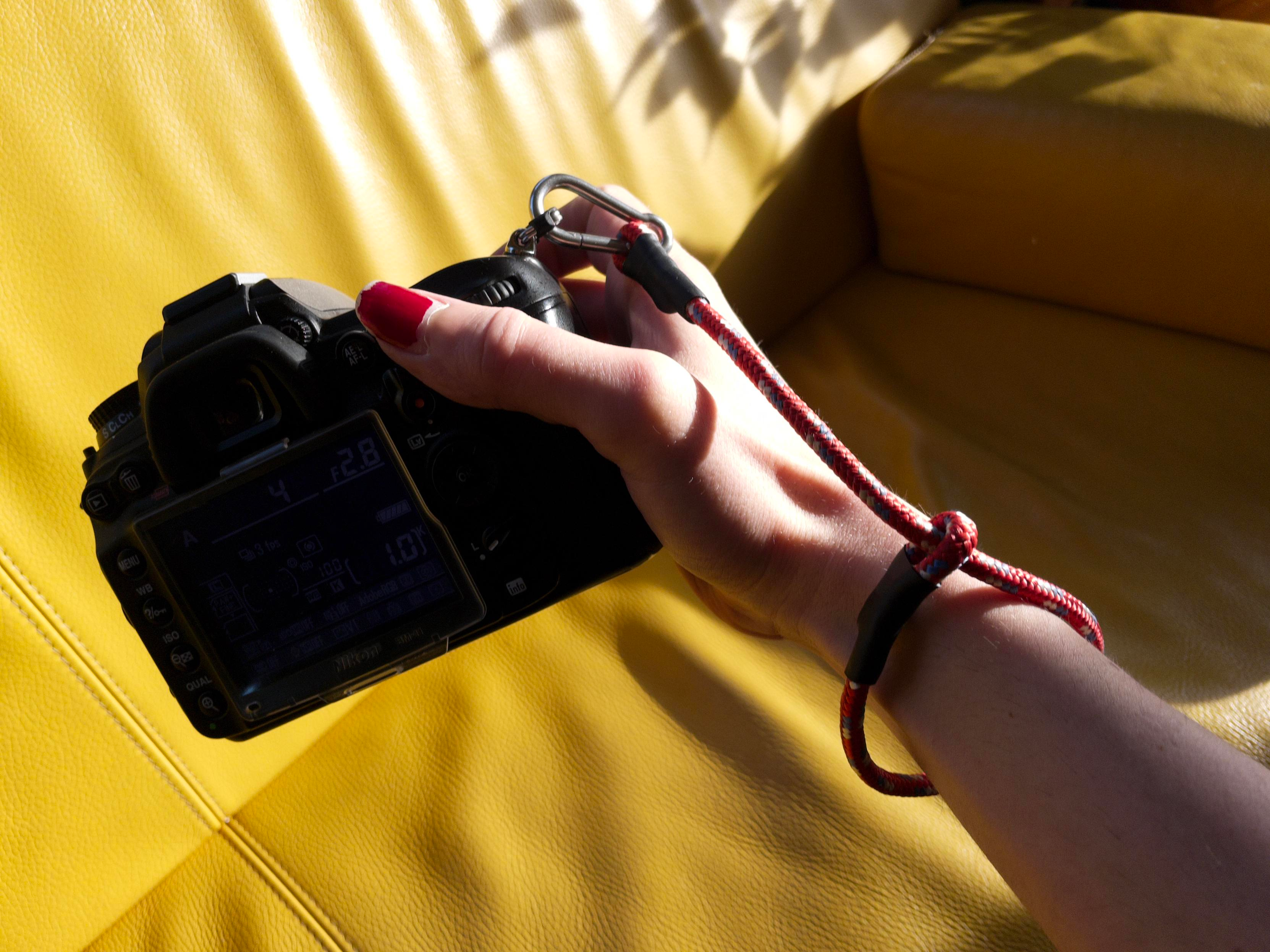 I'm holding my camera with the new strap attached. The rope is around 5 mm thick, and red with blue and yellow details woven around a fiber core. 