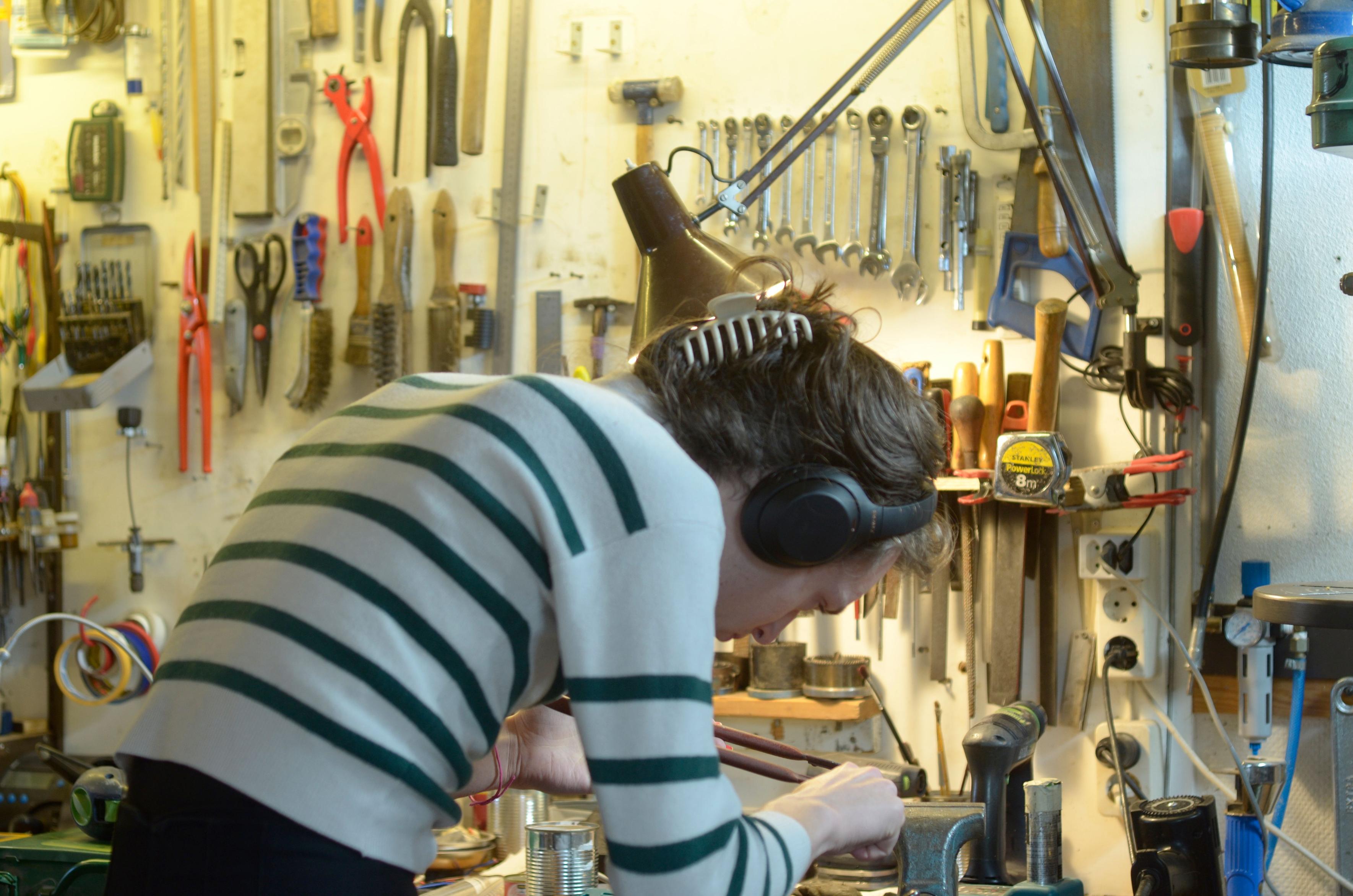 Me sawing out a piece of copper but you can't see that because it's behind my hand. I'm wearing a green-white striped top, black headphones, my hair is put up with an ugly beige clip.