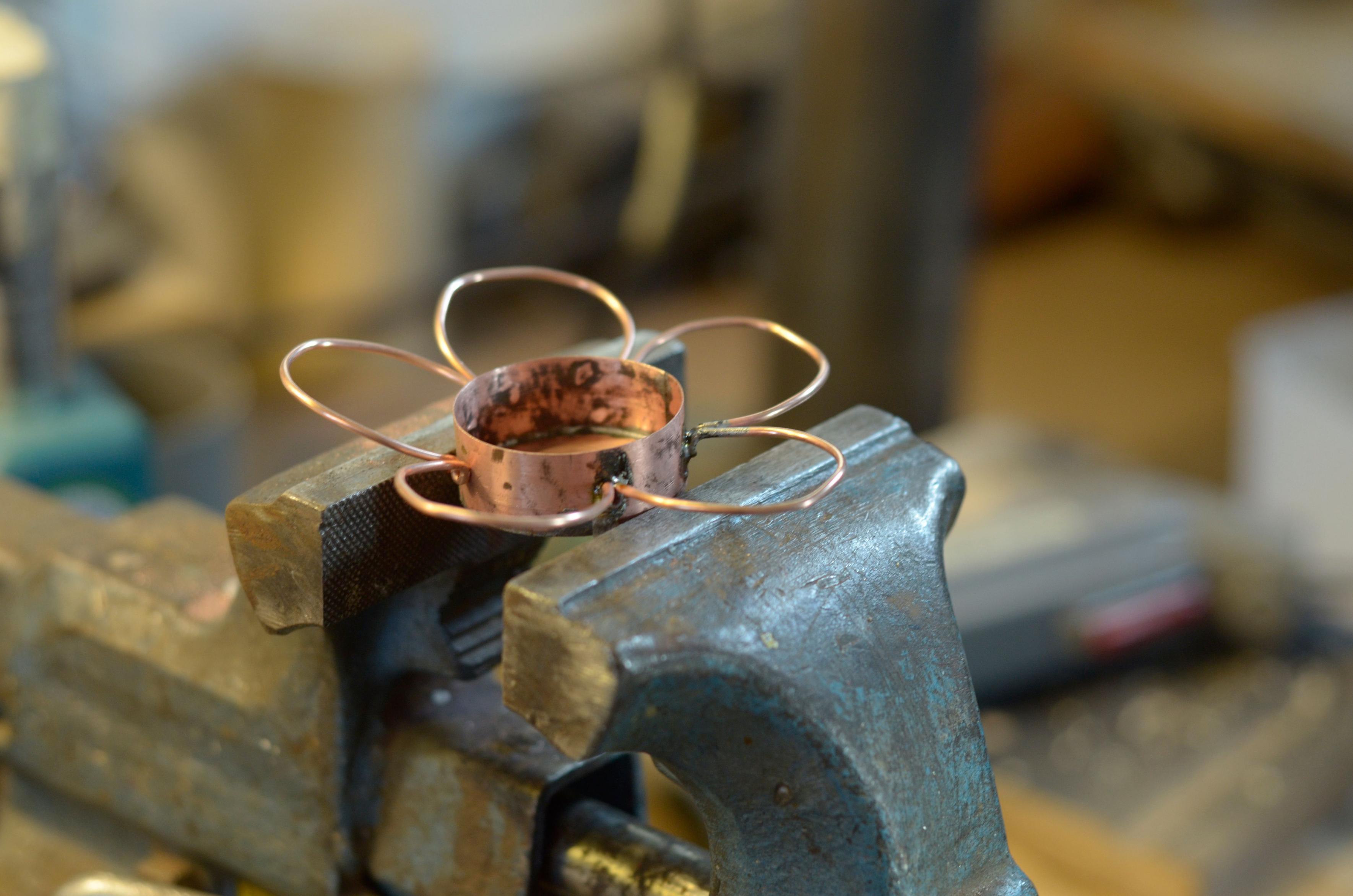 The petal crown soldered onto the rim of the tub, held in the bench vise.