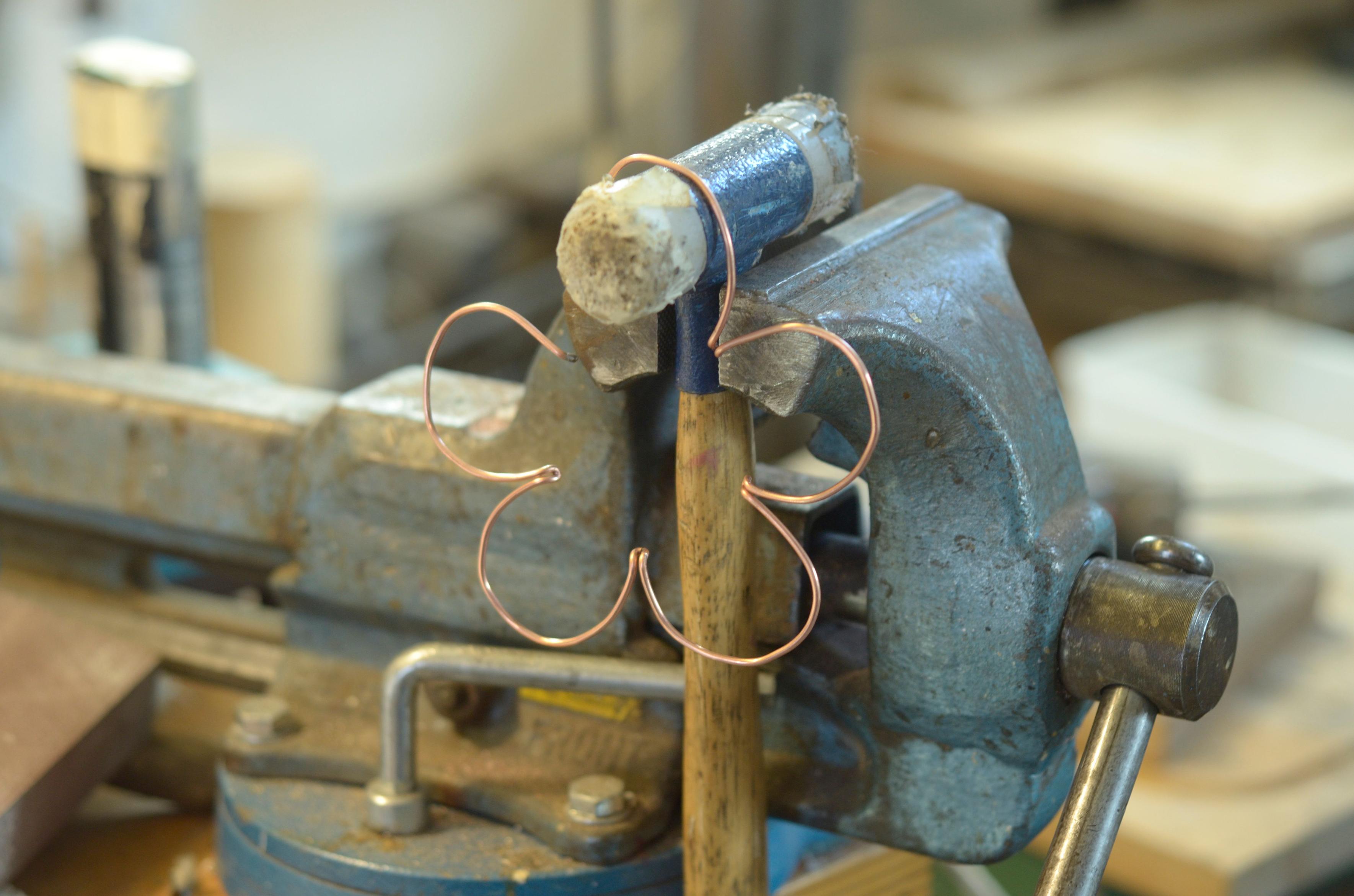 Shaping the flower petals on the round section of a soft plastic mallet held in the vise. There are five petals.