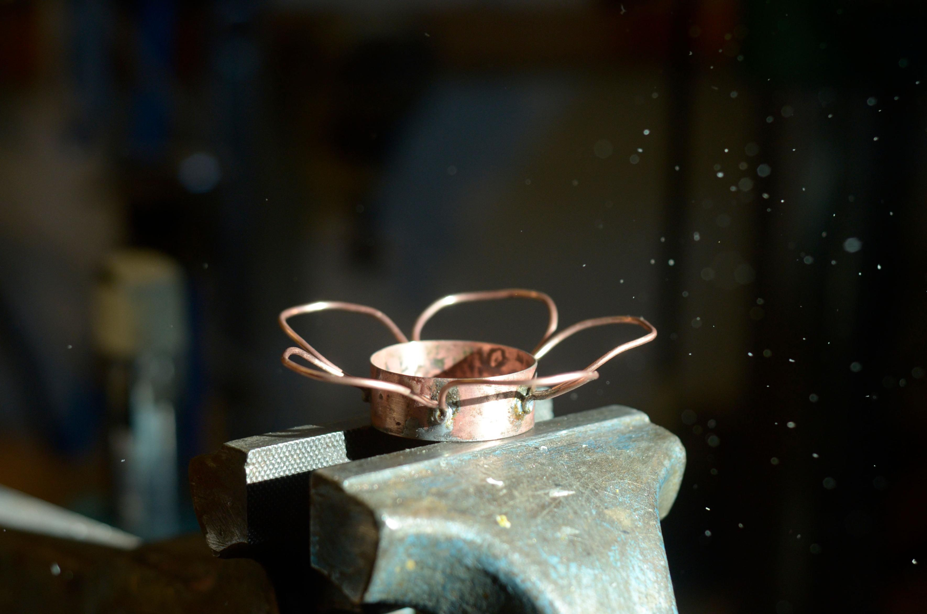 The candle holder sits on top of the vise, empty. It's covered in solder flux gunk. Beautiful dust specs fly in the air as they are hit by the sunlight illuminating the scene.