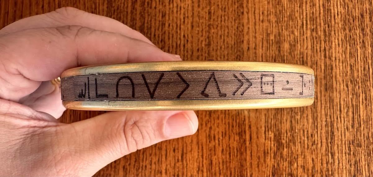 The wooden veneer around the outside of my brass puzzle box, with toki pona laser etched into it.