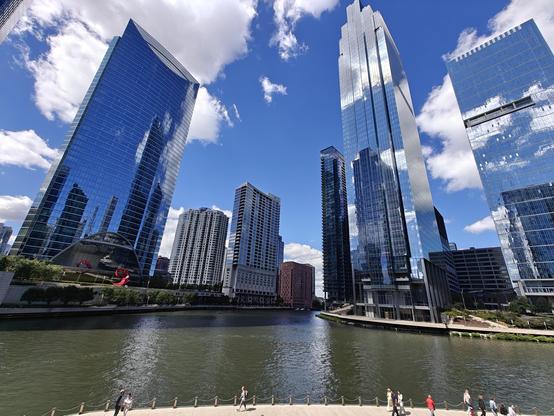 Tall building during the day. Blue sky and clouds reflect from the buildings. Water below.