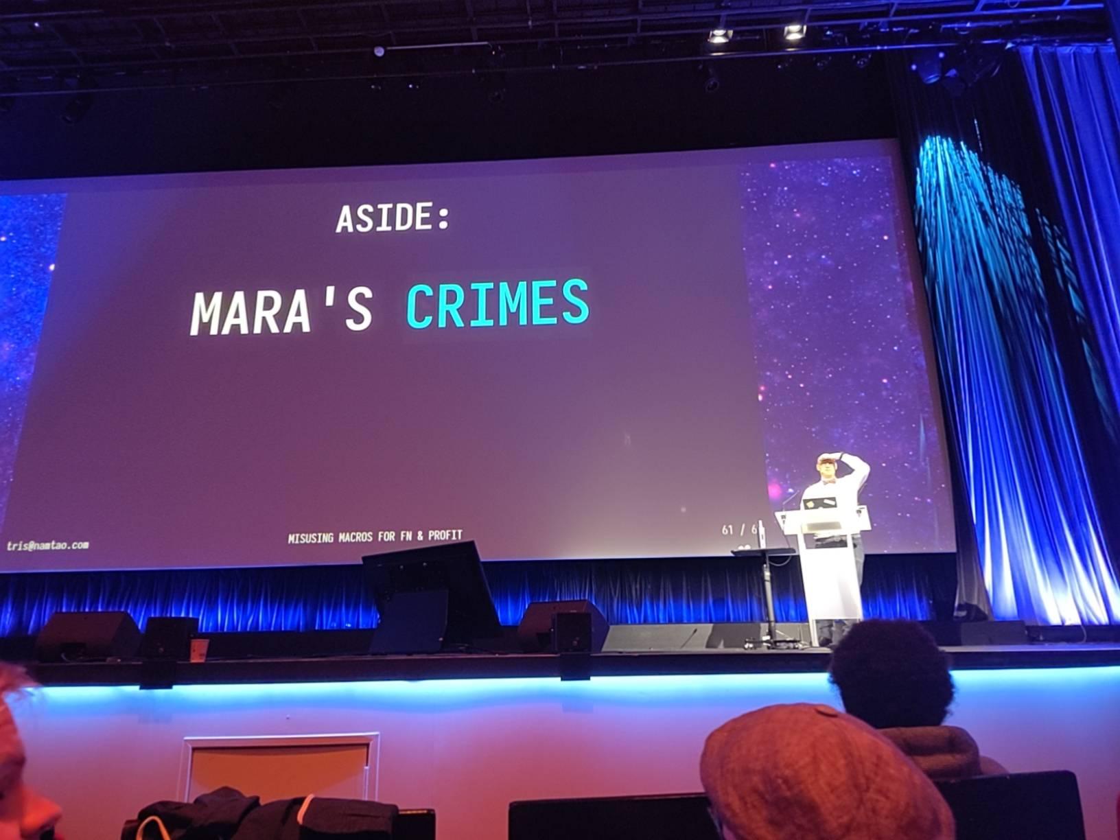 Tris on stage at Eurorust with a slide displaying "Mara's crimes" in big letters behind him.
