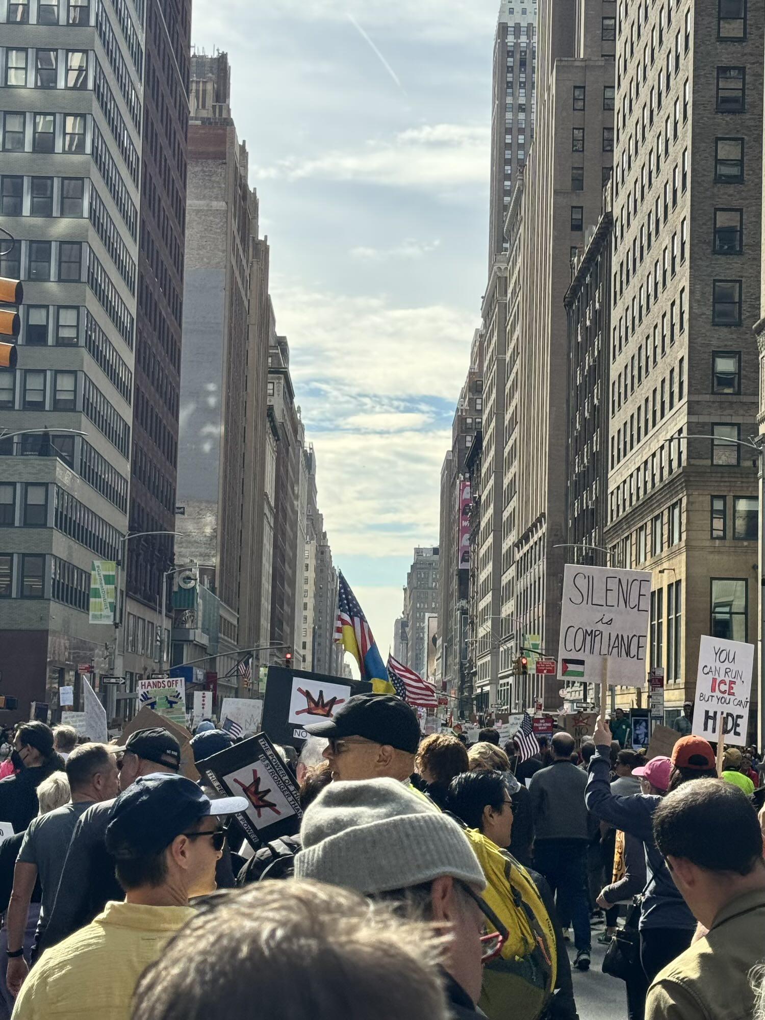 A photo of a large crowd in NYC at a protest featuring a sign that says “silence is compliance” and another that’s a half US half Ukrainian flag