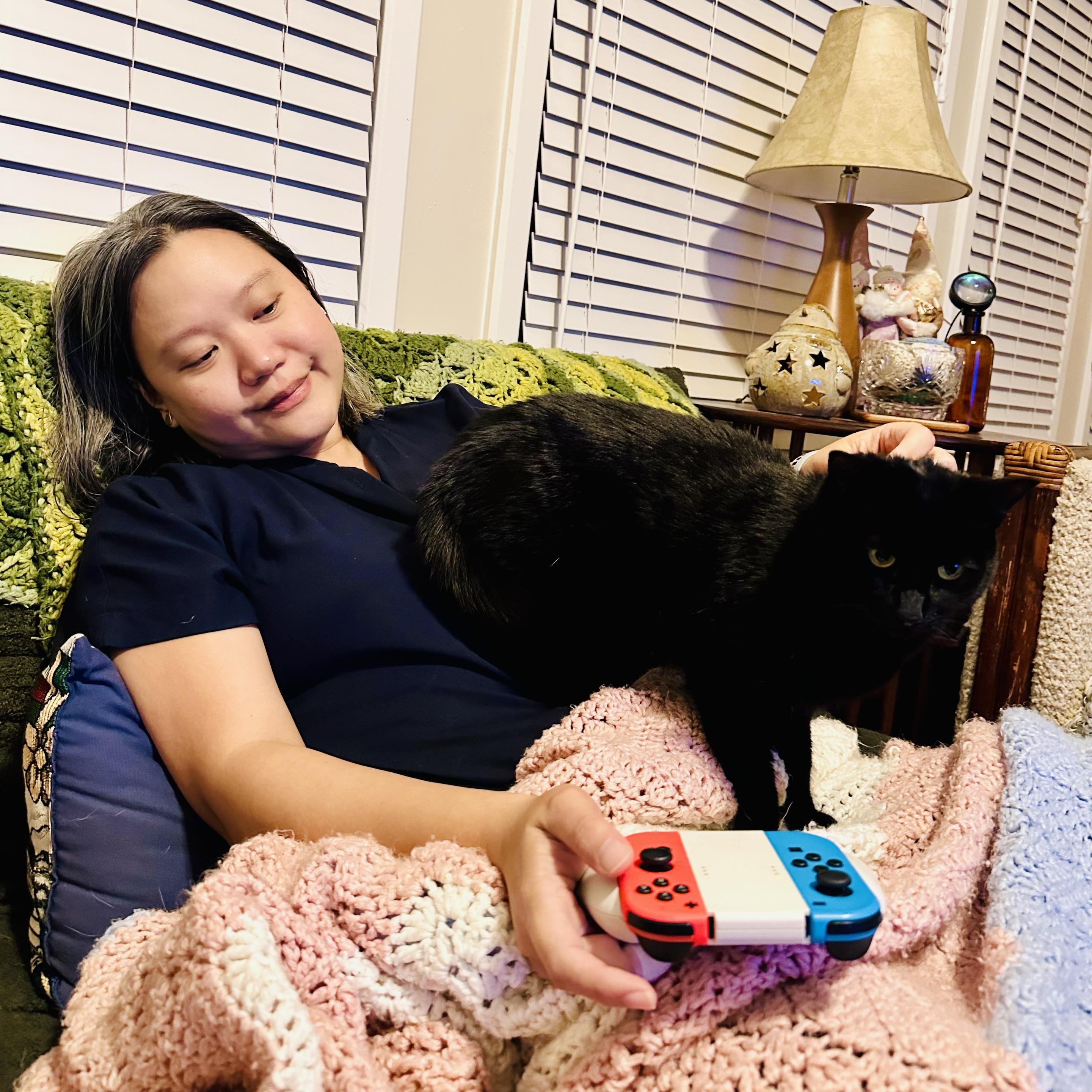 Photo of me holding a Nintendo switch controller
While a little black cat tries to sit on me