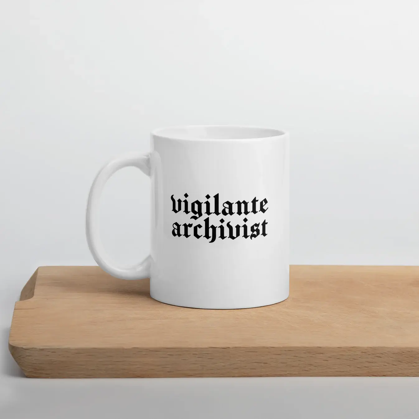 A white mug with “vigilante archivist” in black blackletter type