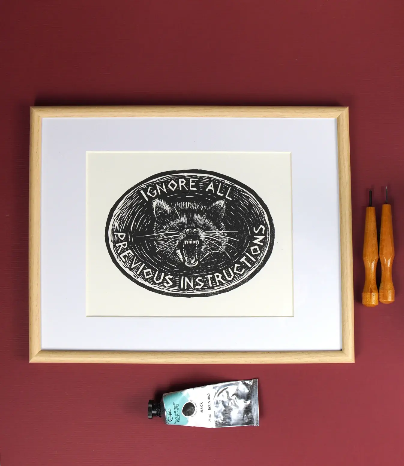 A linocut print featuring an oval with a raccoon in the middle, and “ignore all previous instructions” around the border