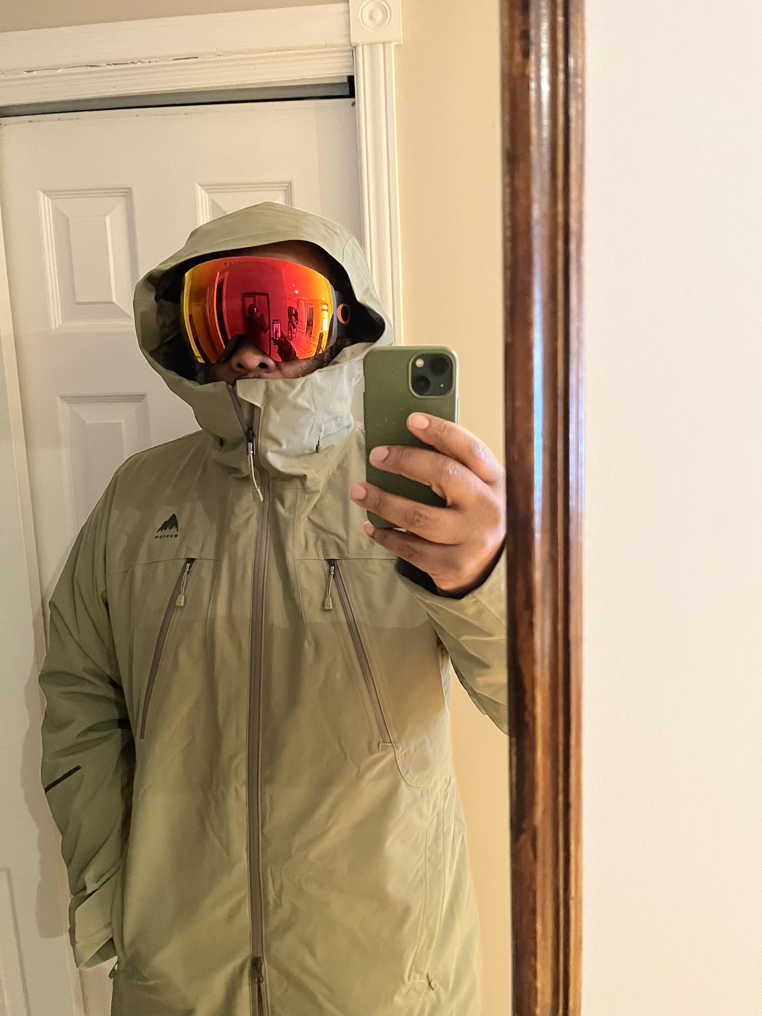 mirror selfie wearing light green winter jacket and bright red wraparound snow goggles