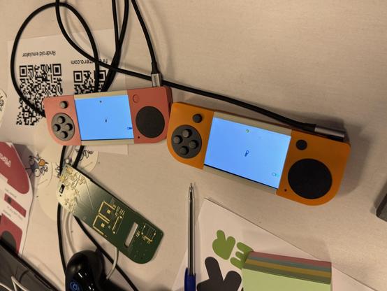 Photo of two game console prototypes next to each other. There is also an empty PCB next to them. 