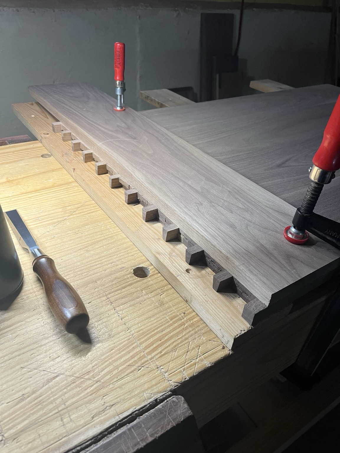 A walnut board laying across the end of a large walnut panel. The edge shows tails cutout for dovetail joints.