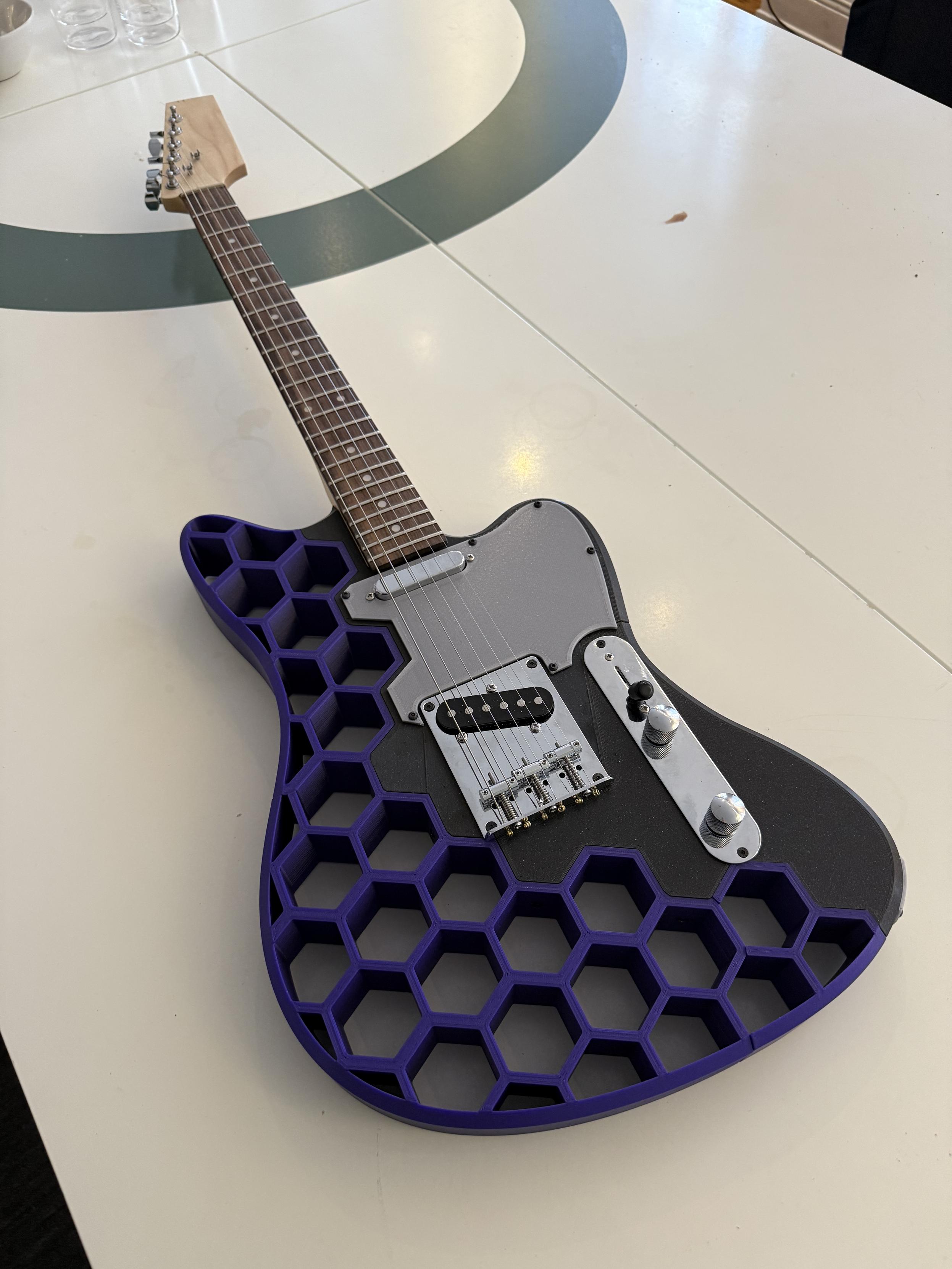 Photo pf a purple and black 3D printed guitar laying on a white table.