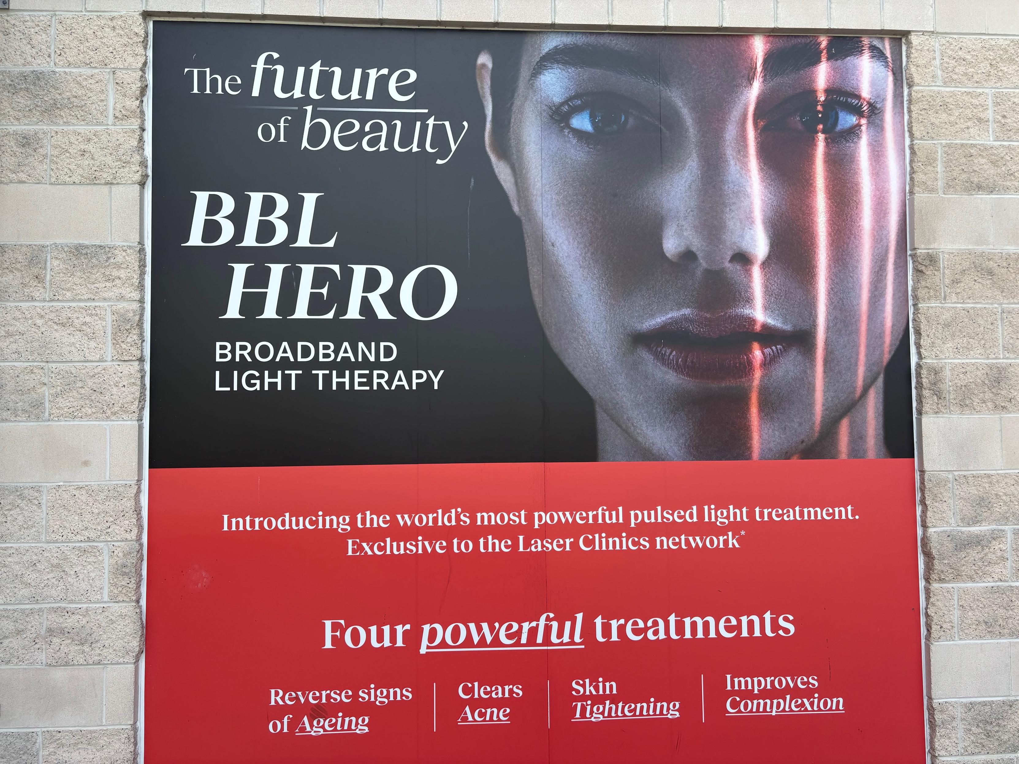 A billboard prominently displayed on the wall of a popular shopping mall. The ad has a photo of a blemish-free and wrinkle-free  face with the quote "The future of beauty". The ad promotes "BBL Hero" aka "Broadband Light Therapy" with the claim: "world's most powerful pulsed light treatment. Exclusive to the Laser Clinics network*".

The "*" is doing a lot of heavy lifting here and is not further explained, natch.

The ad further claims that this broadband technology provides "Four powerful treatments": "Reverse signs of ageing", "Clears Acne", "Skin Tightening" and "Improves Complexion".