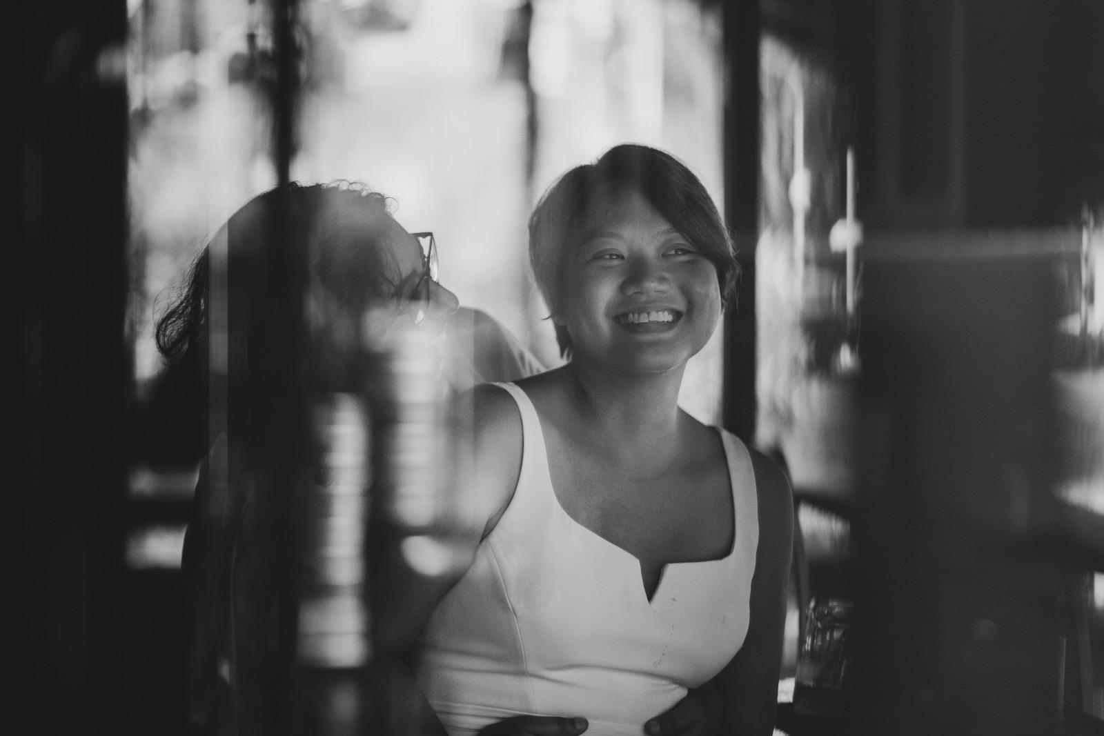 A scan of a black and white film photo of my wife (obscured) holding me while I’m in a white dress