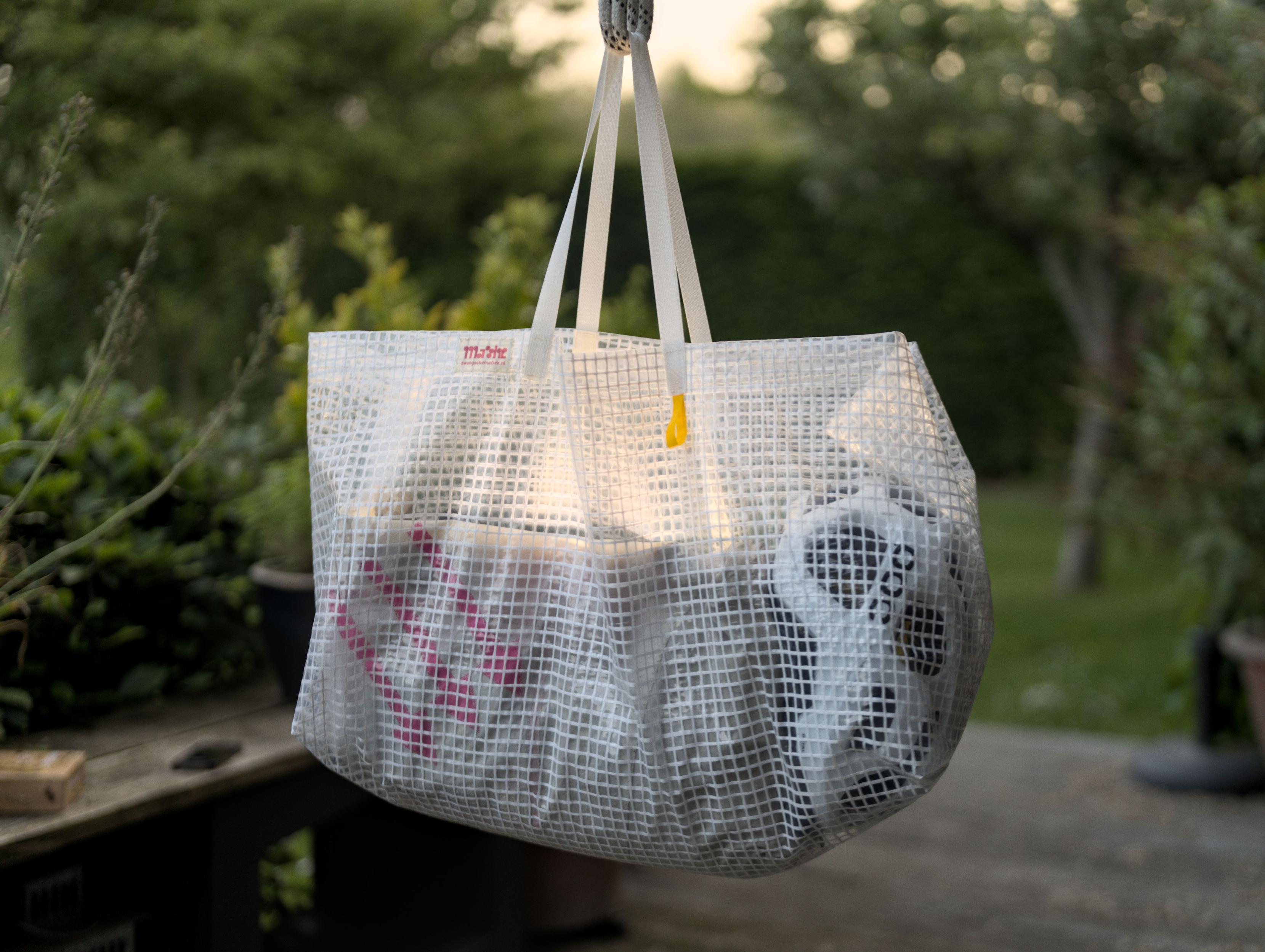 A large bag made of a transparent material fortified
						  with white fibers hangs on a rope in a garden. You
						  can see my backpack and bike helmet through the walls
						  of the bag. On the top rim are my label and a yellow
						  loop is attached right under the handles. The handles
						  are made of a white webbing. I placed a lamp inside
						  the bag to make the photo look cool. As a result,
						  this photo looks extremely cool.