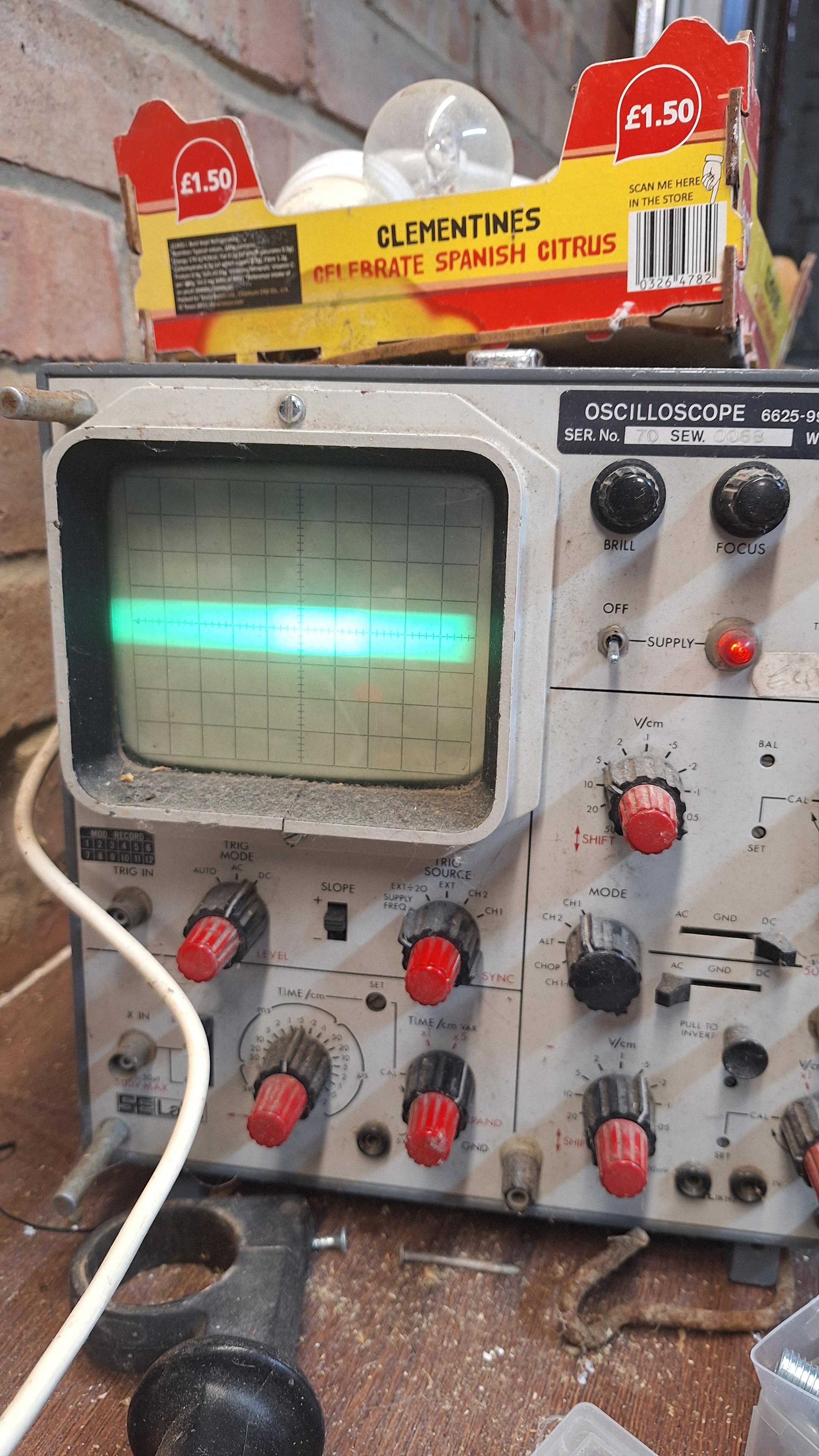 Front of Oscilloscope showing various knobs and switches and screen with fat green bar on it.