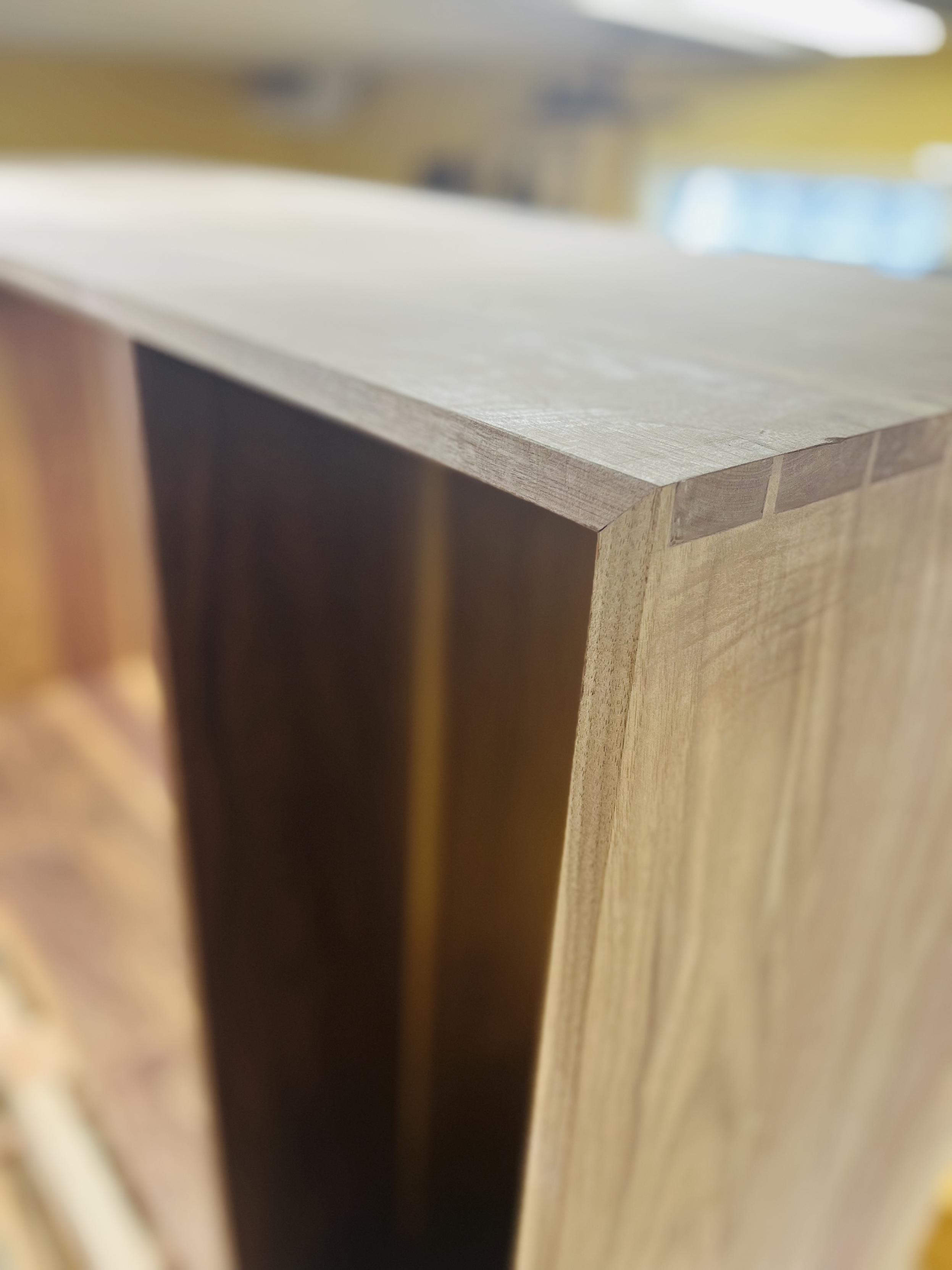 A close up of a corner to a walnut cabinet. The corner is a mitered joint with the inside edge showing dovetails.