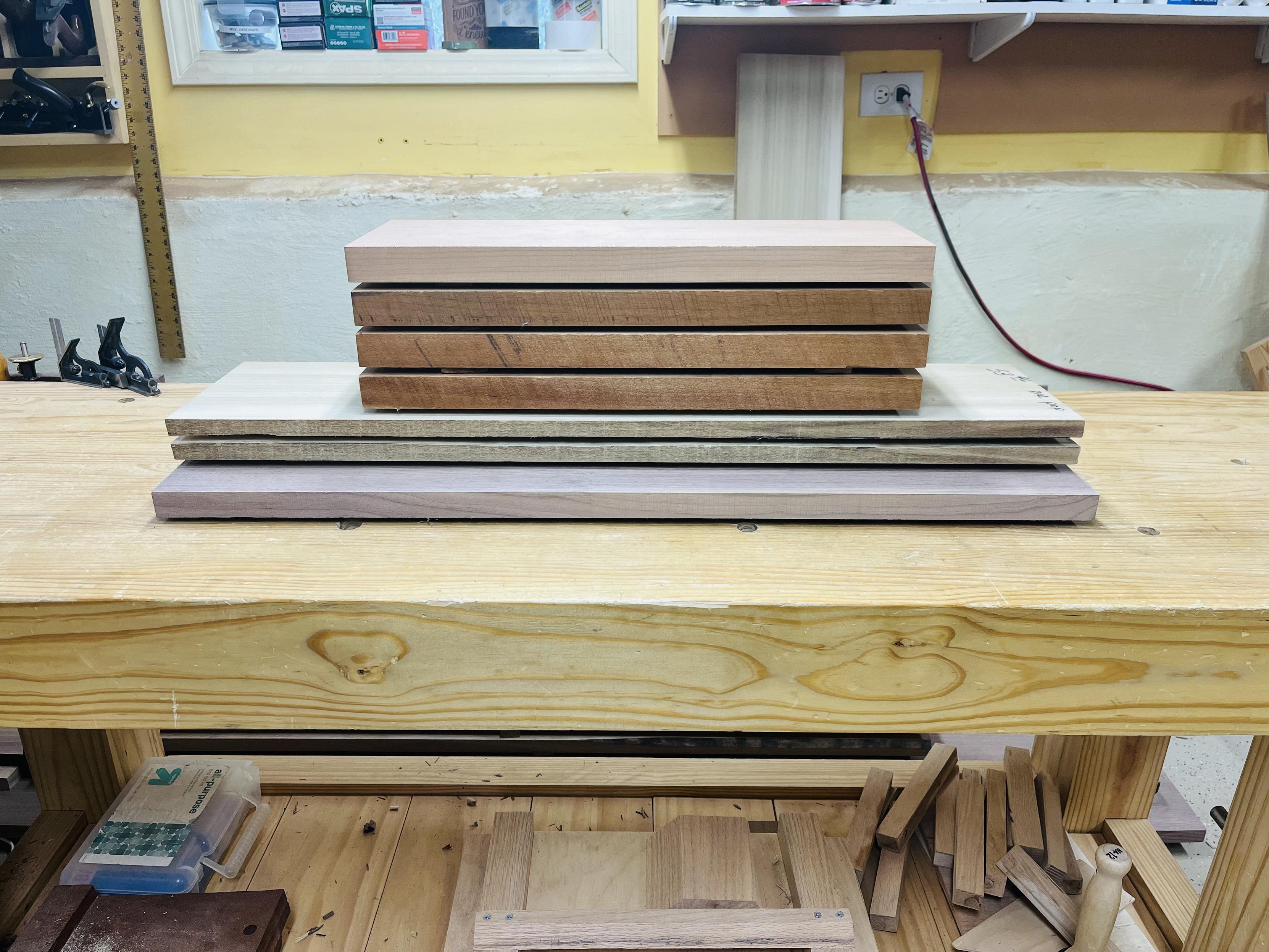 A stack of wood at various lengths on top of a woodworking bench.