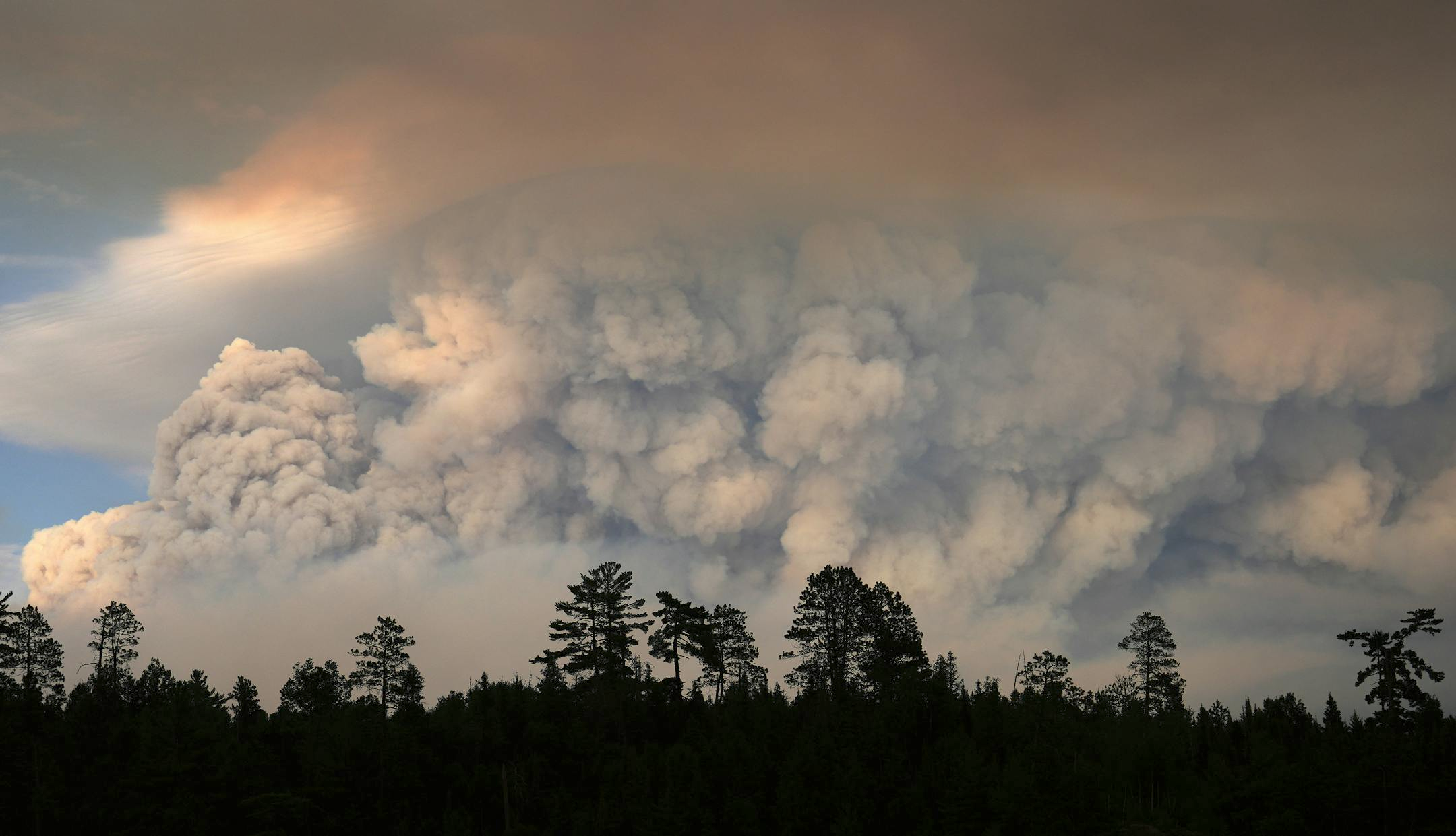 Smoke billows above a darkened treeline of conifers. Glimpse of blue sky and clouds.

Plumes of smoke from the Camp Fire hangs in the air on Moose Lake as multiple wildfires burn in the Boundary Waters Canoe Area Wilderness. The fires prompted the closure of the BWCAW and evacuation of campers on July 14. (Anthony Soufflé/The Minnesota Star Tribune)