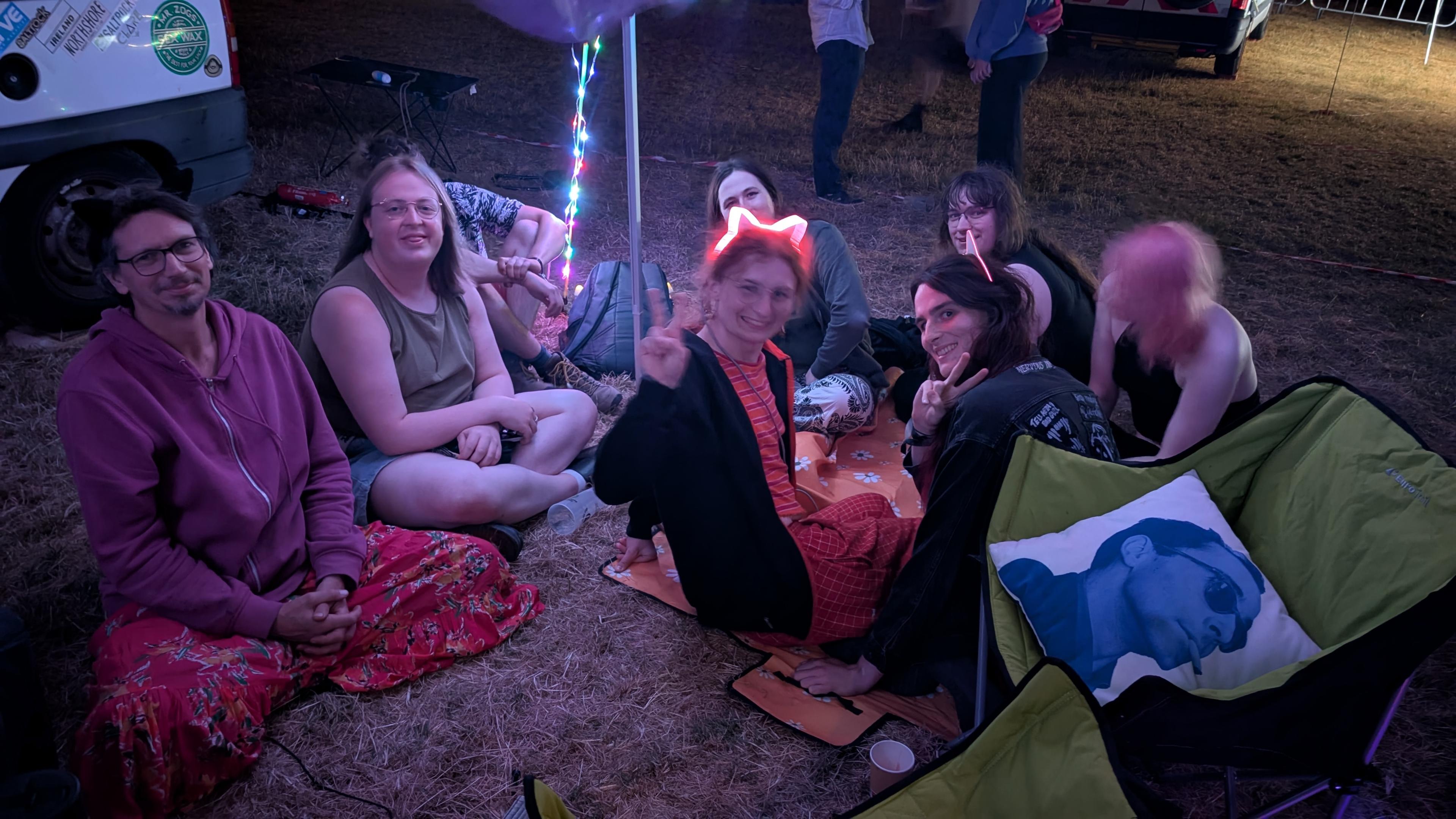 a group of people sitting on a blanket on the ground at night. one is wearing cat ears