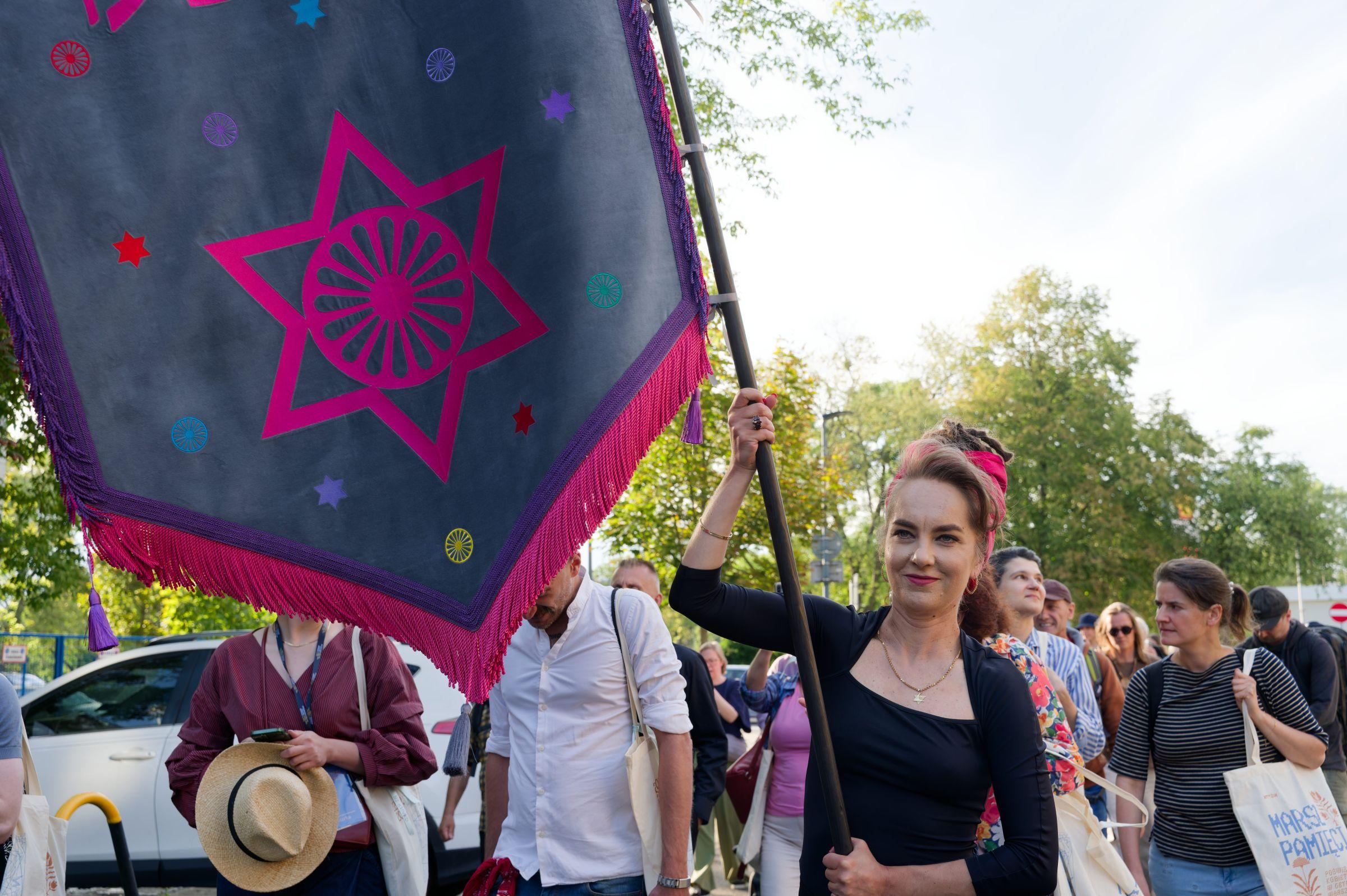 Arist and activist Zuzanna Hertzberg leading the March of Remembrance on the streets of Muranów district in Warsaw, carrying a pink and grey banner with the Star of David.