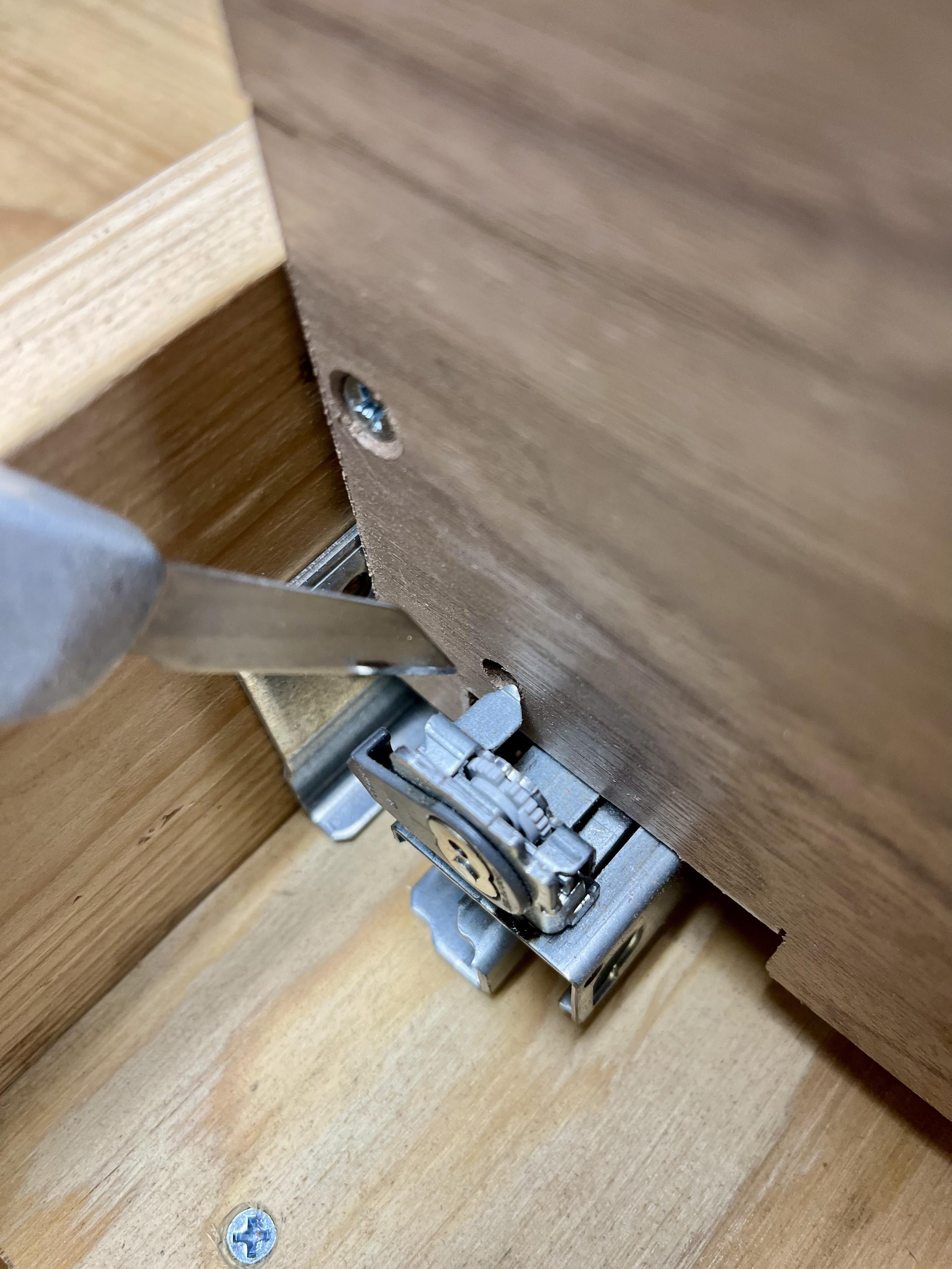 The back of a wood box with a small knife pointing the the slider track that has tabs sticking towards the box. The box has holes that line up to them but they do not fully sit.