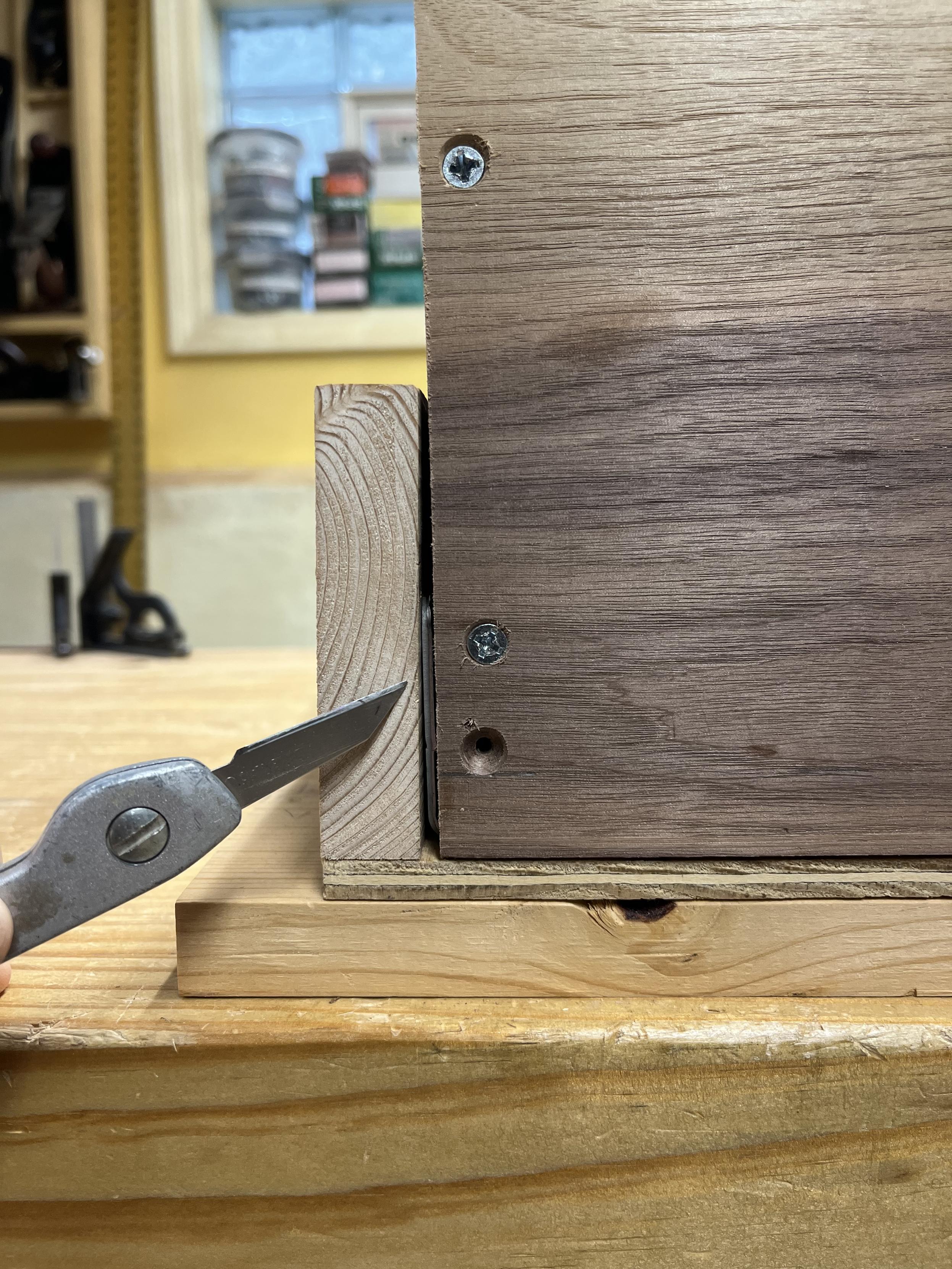 A small utility knife pointing at a 1/8" gap on the side of a drawer showing a little bit of metal where the drawer slide sits.
