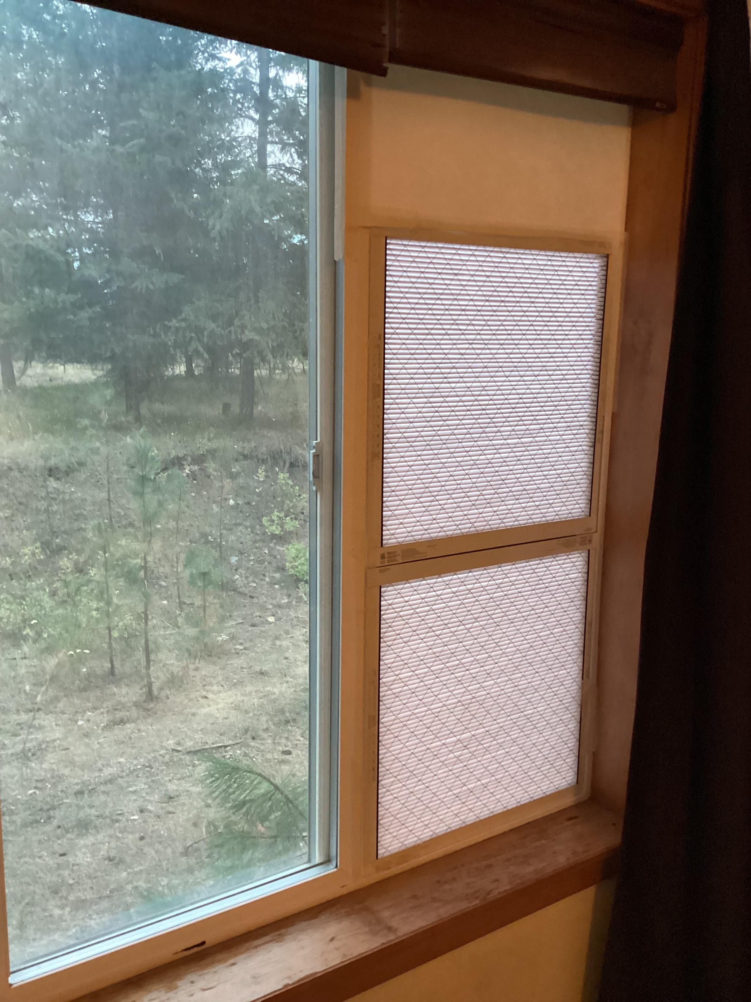 View of the smoky outdoors behind a window, which is opened with two furnace filters stuck in the opening and the top covered with construction paper.