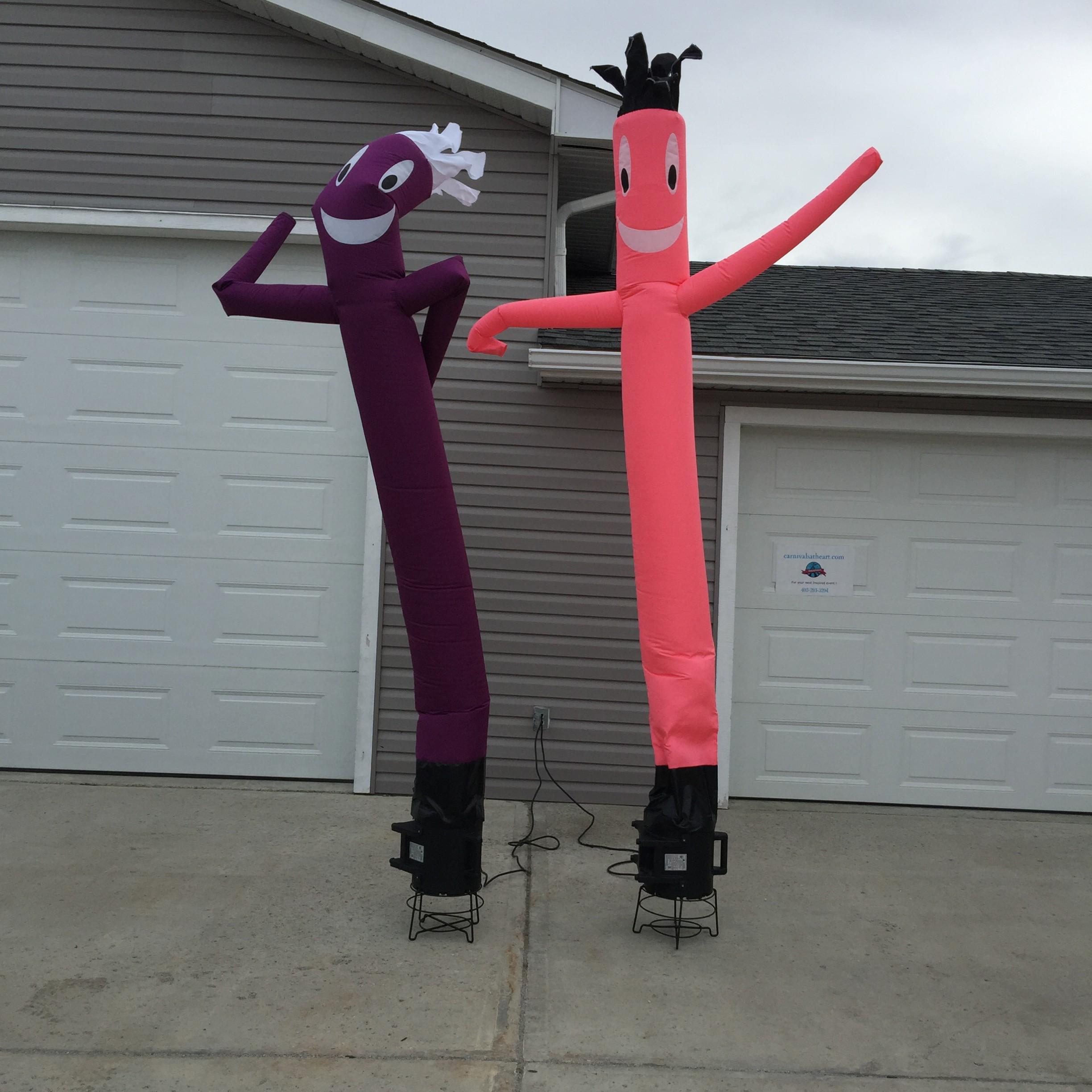 Two wacky waving inflatable tube men in front a suburban house. One is pink-red and one is purple-red.