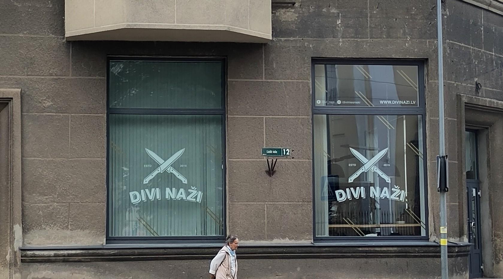 A pair of shop windows, both painted with crossed knives and the words Divi Naži. Which means 'two knives.'