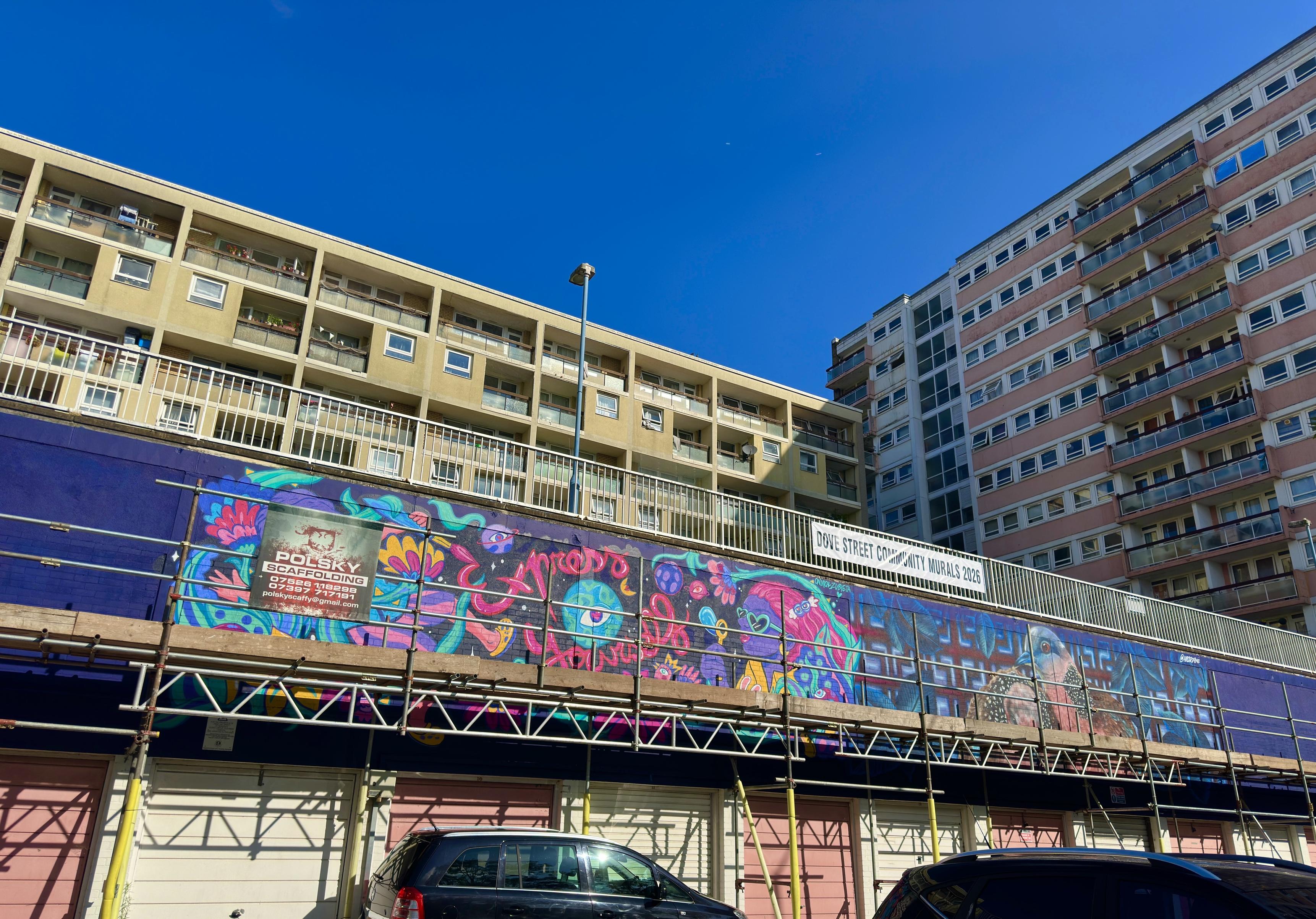 A wall of murals going up: purple and orange paint on a black background