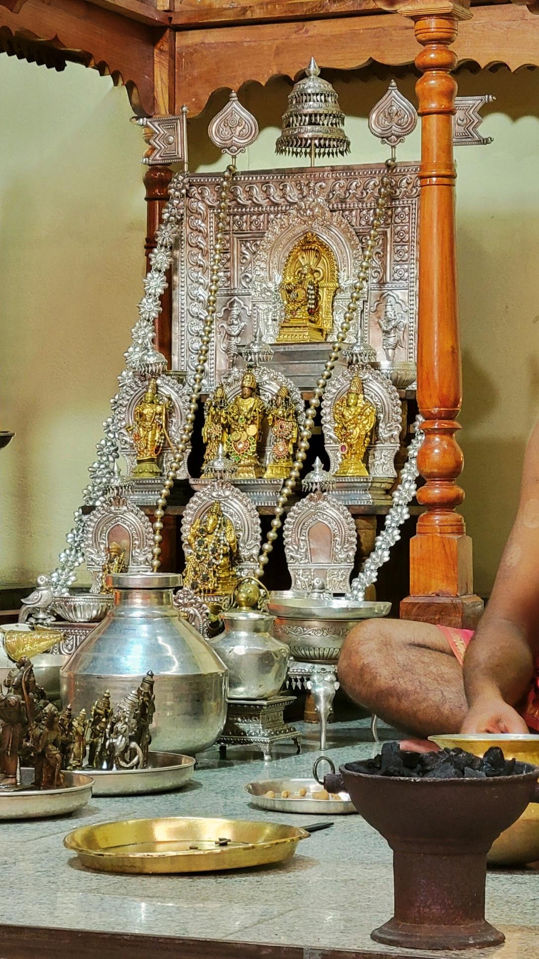 Ornate silver Hindu altar with many bejeweled copper idols. Other silver and copper idols and utensils used in ritual service are placed in front of the altar.