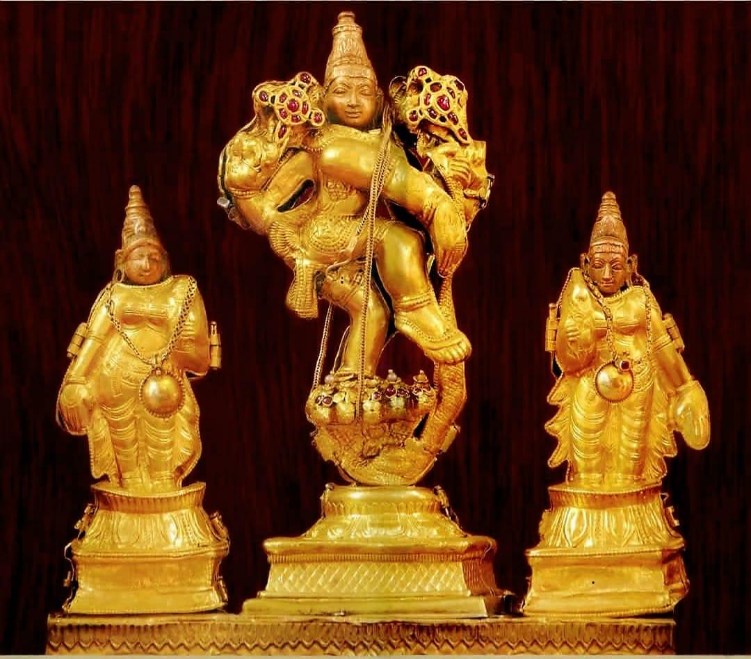 Closeup of three gold-clad idols of Hindu deities. In the middle is 4-armed Krishna ("chathurbhuja kaaleeya mardhana krishna") dancing on the hood of a 5-headed serpent. On either side of him is a feminine idol. All three idols are placed on a gold pedestal.