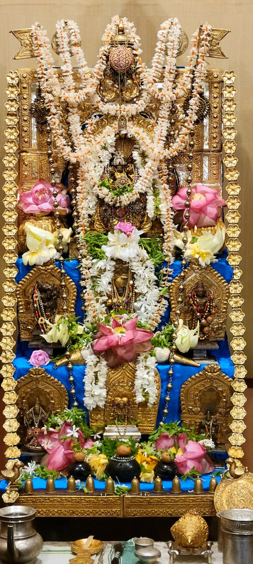 Closeup of a Hindu altar. The altar is stepped with multiple idols at each step. A garland of gold flowers on the altar. Jasmine strings and pink lotuses on the altar.