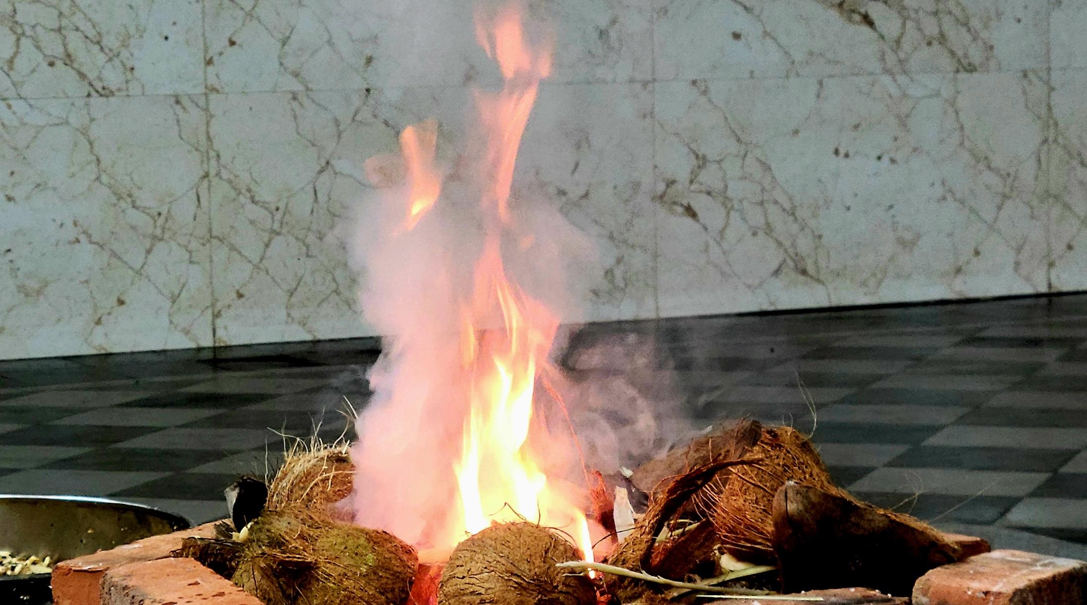 Closeup of red and white flame coming out a fire pit. Dry coconut half shells at the top of the pit.
