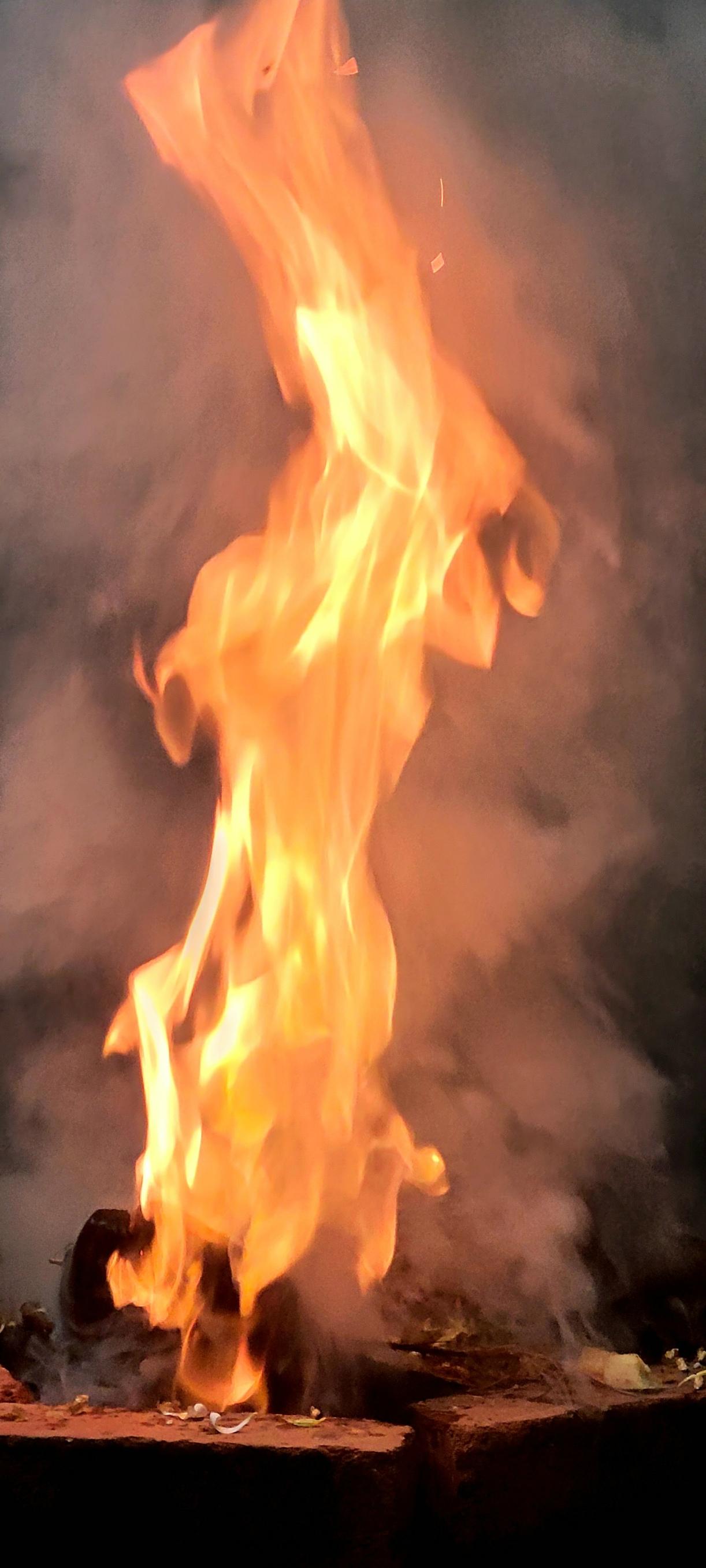 Extreme closeup of a high red and white flame coming out a fire pit.  White and gray smoke around the flame. Objects in the pit are not discernible.