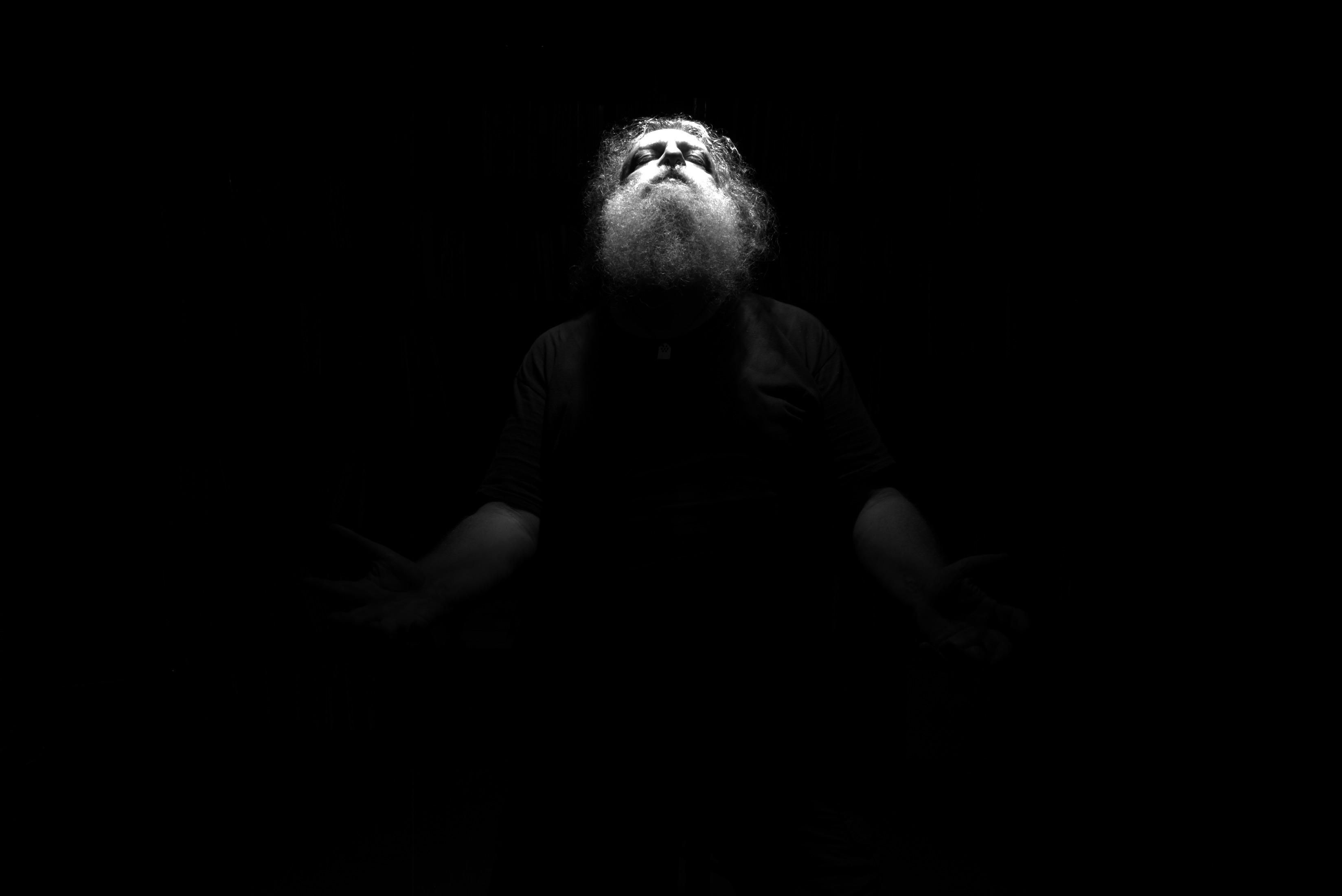 A bearded figure looking up into a bright light. Everything else is darkness.
